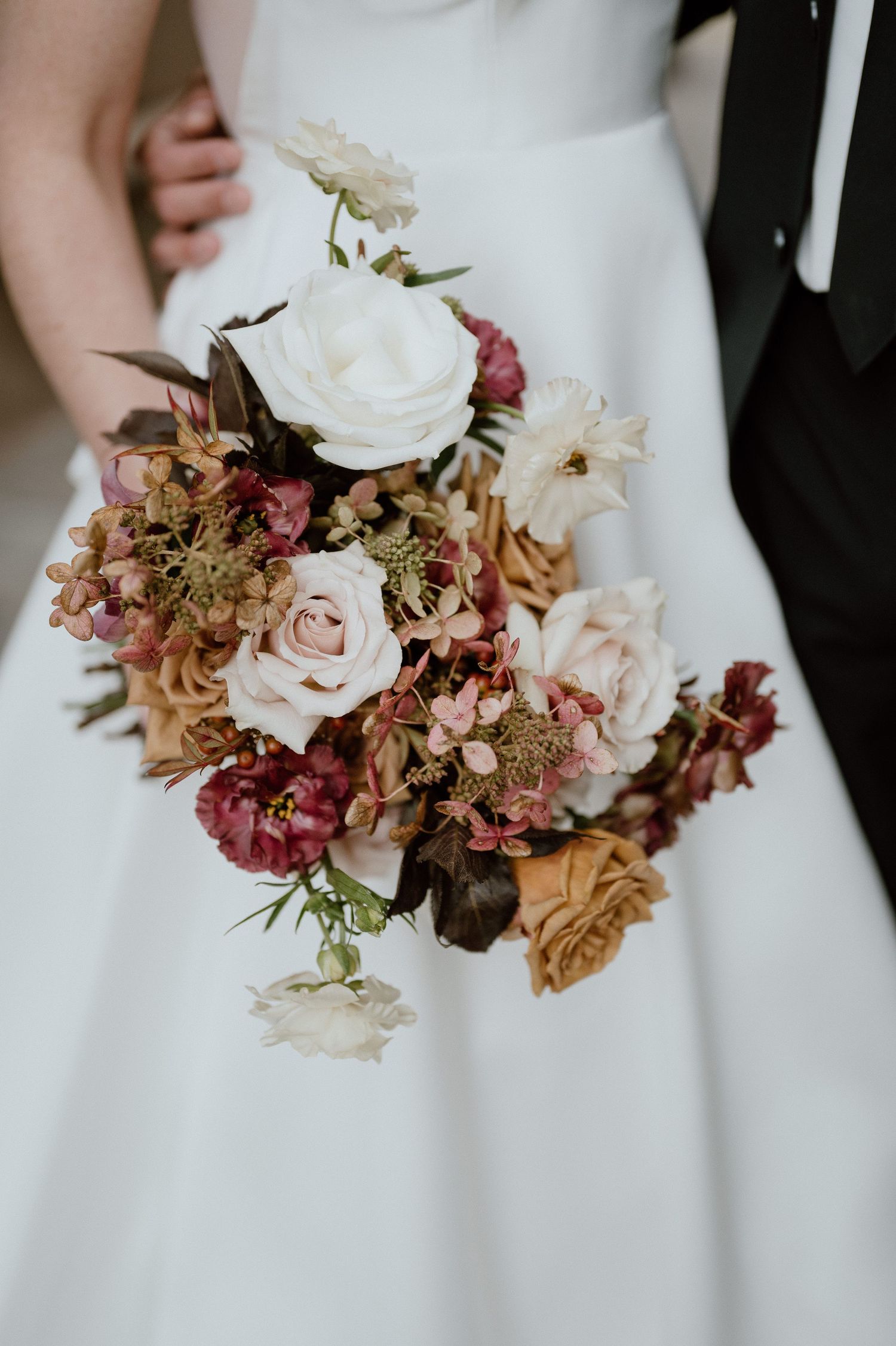 A stunning wedding bouquet featuring white roses and burgundy flowers against a white dress.