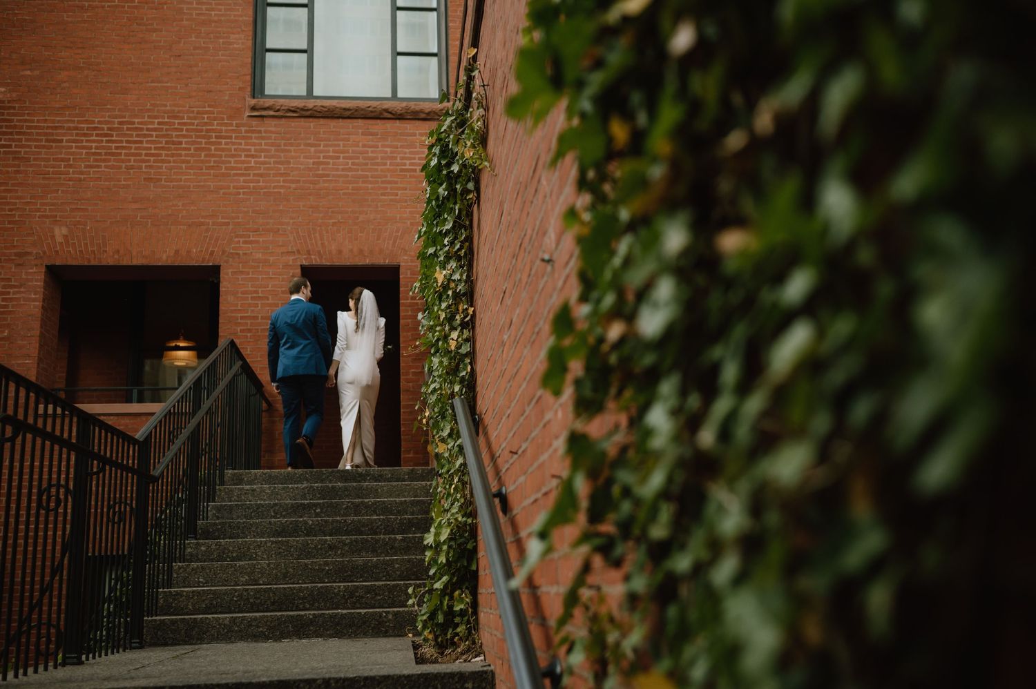 Wedding couple climbing stone steps at a brick building with green ivy.