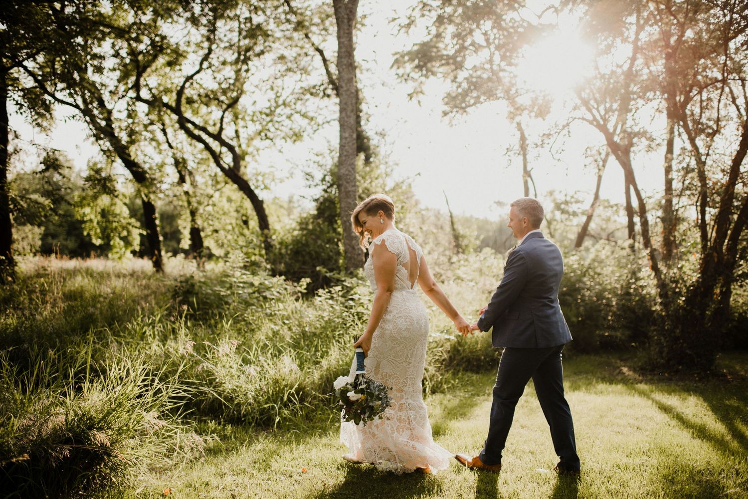 Couple walking through sun-drenched garden path during wedding celebration.