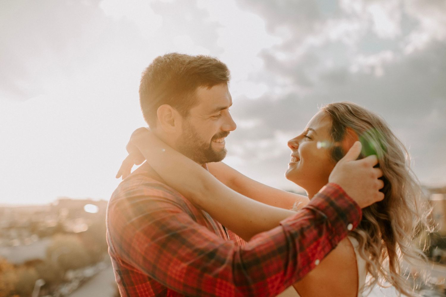 Loving couple embracing on rooftop with warm sunset light and cloudy sky.