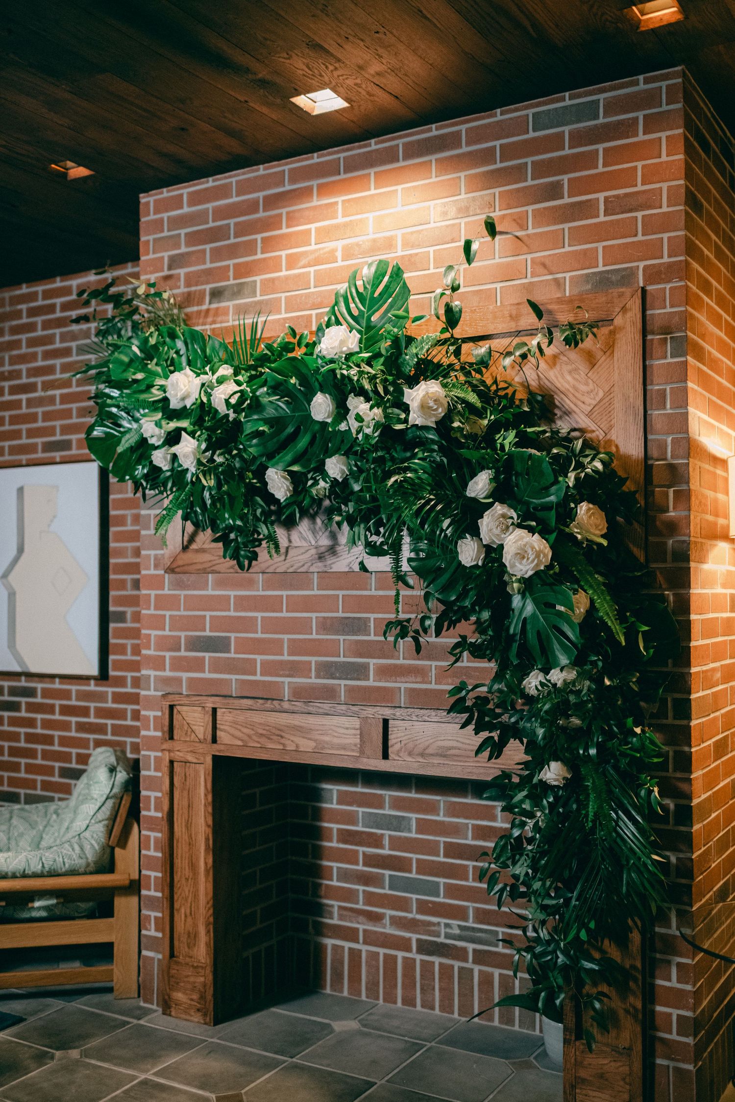 Elegant floral arch with white roses and monstera leaves decorates a brick wall interior space.