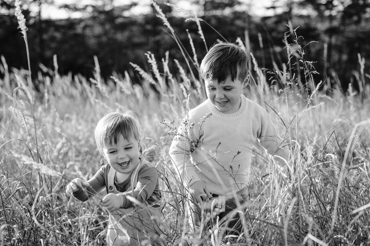 Black and white photo of two children standing together in a field of tall grass.