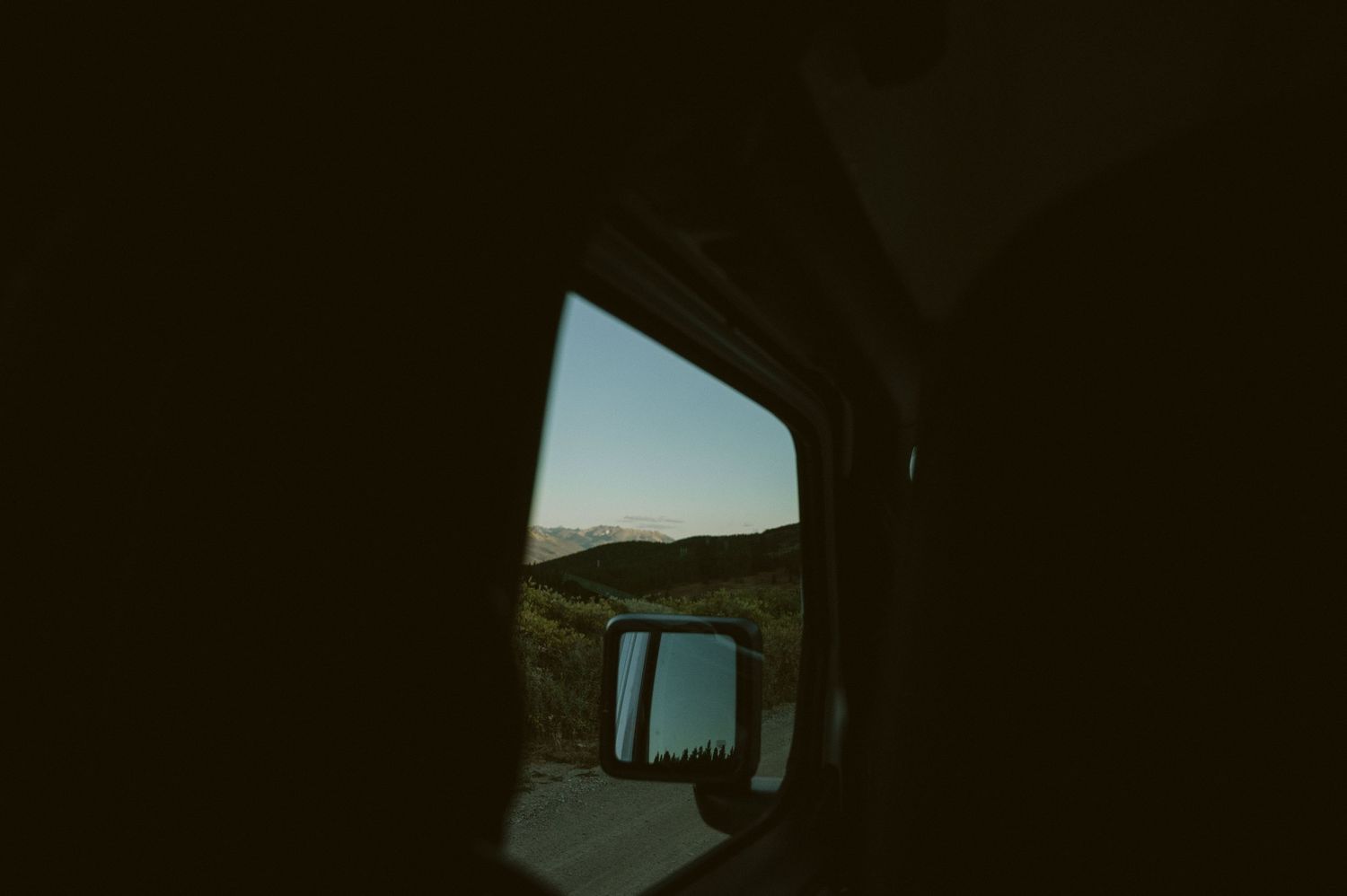 A moody landscape view through a car window while driving through mountains.