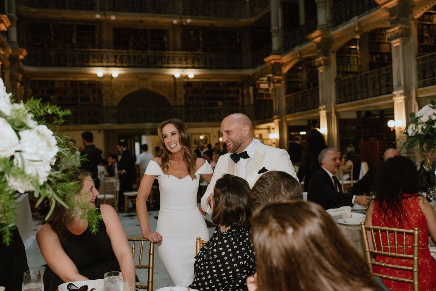Reception guests mingle and celebrate at an elegant library wedding venue with white floral decor.