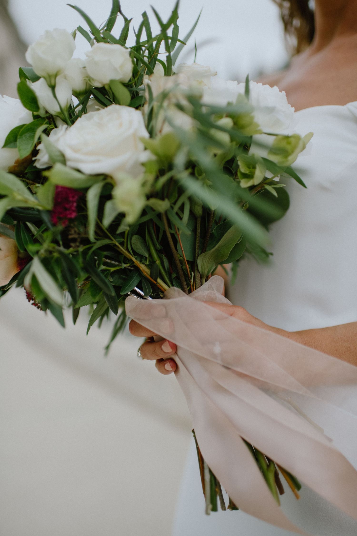 A close-up of a wedding bouquet with white roses, greenery, and delicate ribbon wrapping.