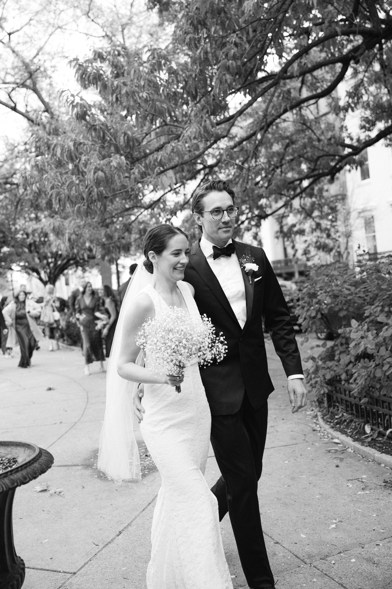 Black and white wedding photo of couple walking together under autumn trees.