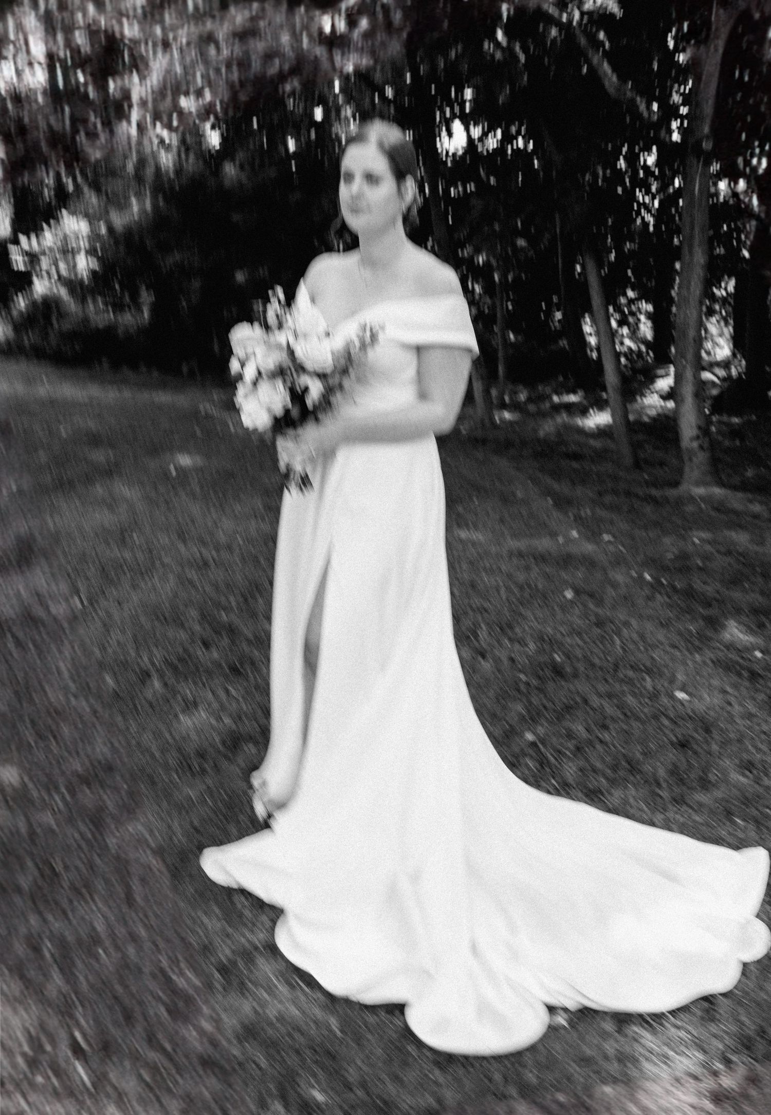 Black and white portrait of bride in an elegant off-shoulder wedding gown holding a bouquet.