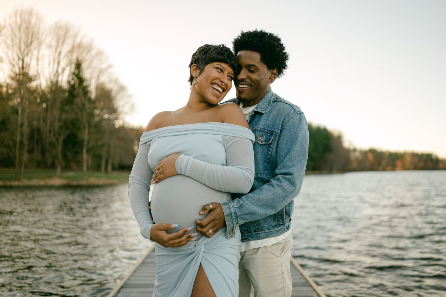 Expecting couple shares a joyful moment by the water during sunset.