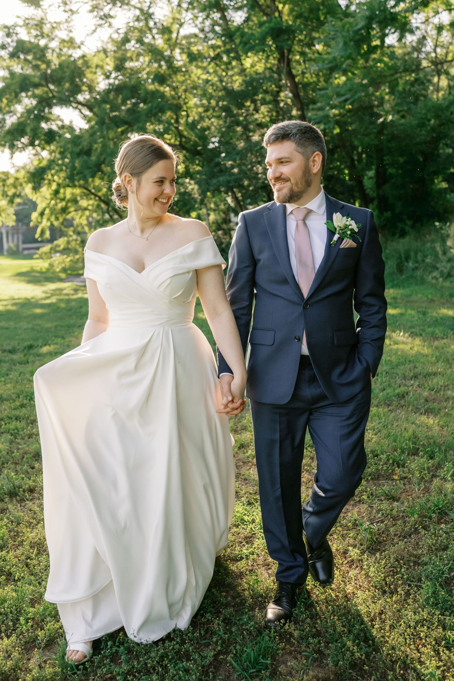 A couple walks together on green grass during a sunny outdoor wedding.