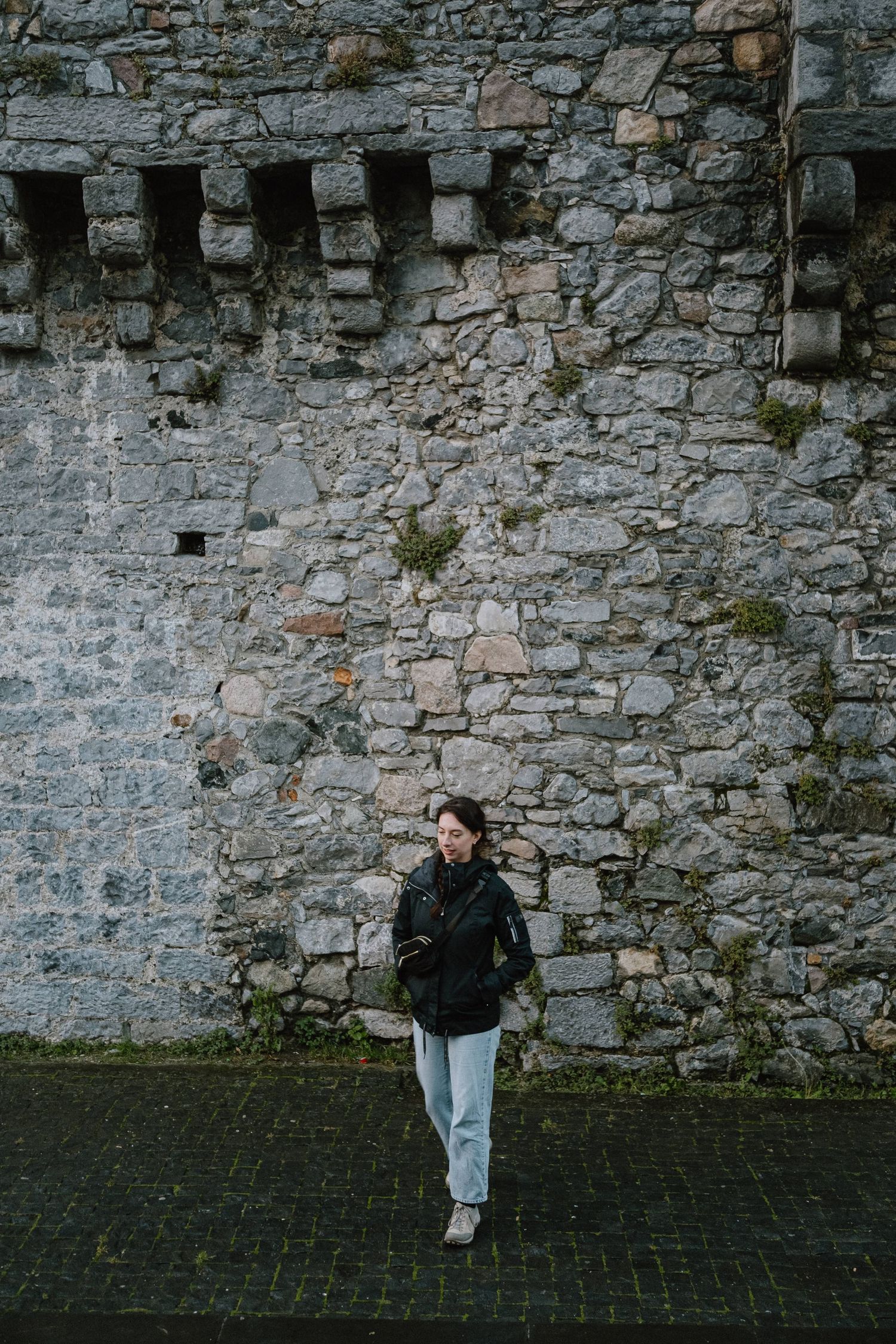 Person standing against ancient stone fortress wall with window openings.
