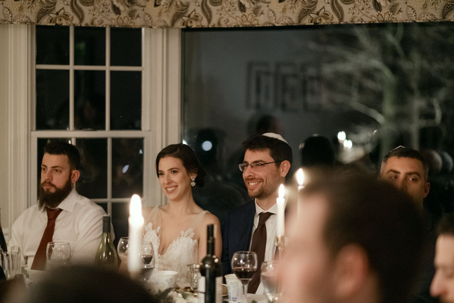 Candlelit wedding reception dinner with guests seated at a long table during speeches.