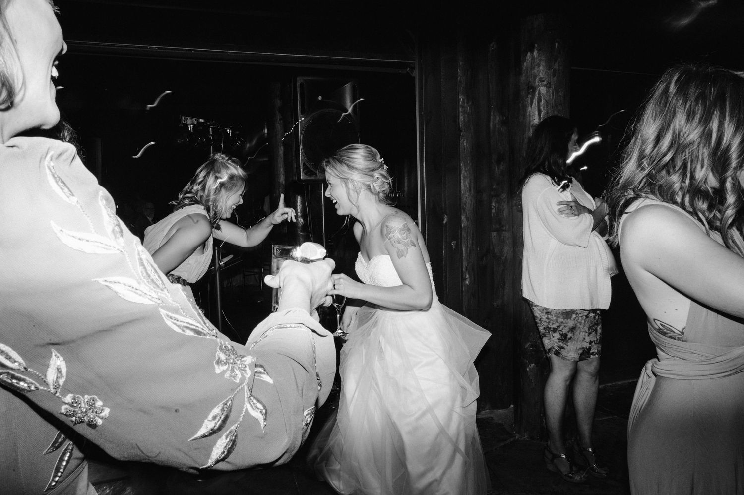 Black and white photo of wedding guests dancing and celebrating at a dimly lit reception.