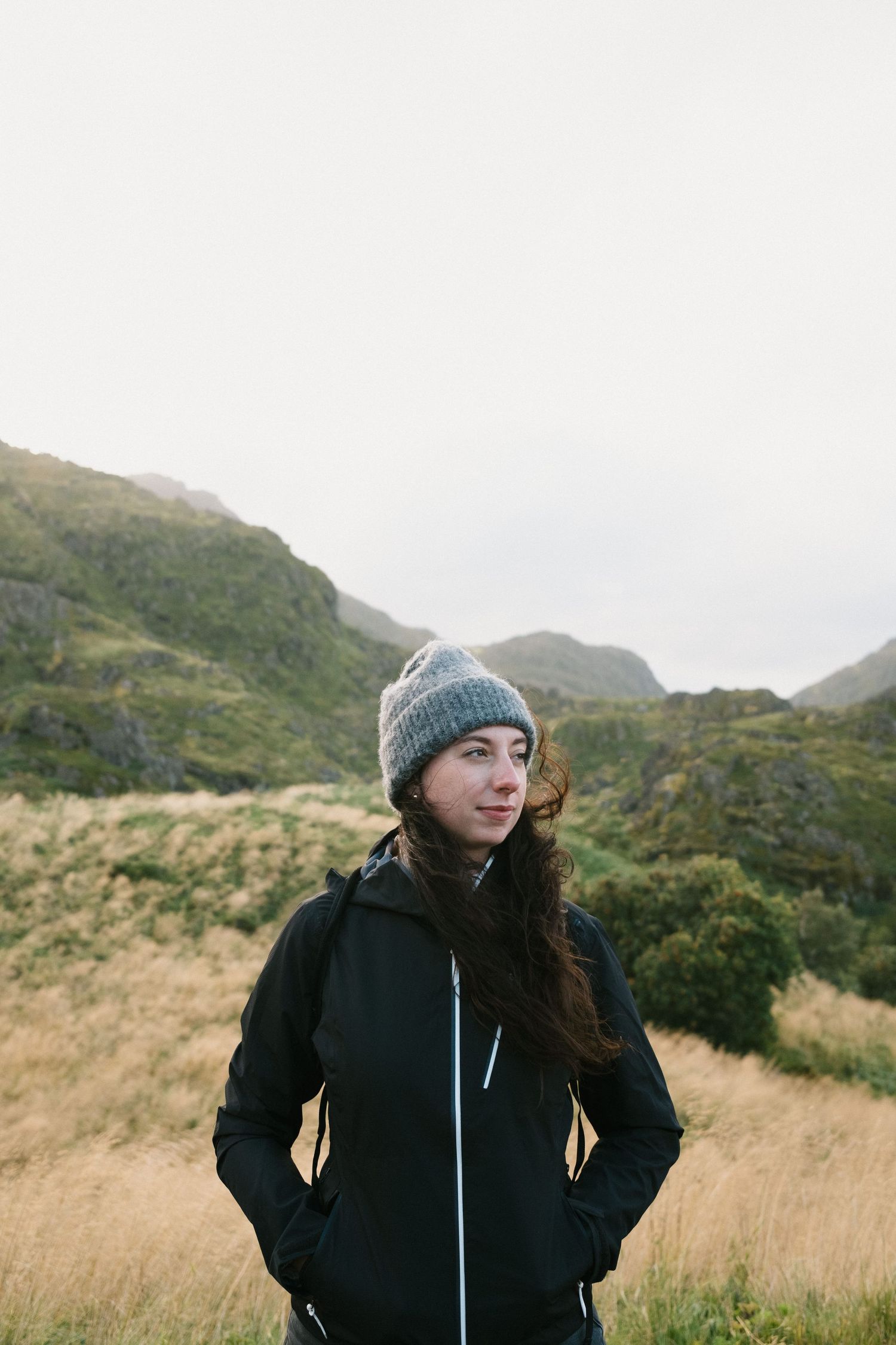 Person in winter clothing stands against backdrop of misty green hills.