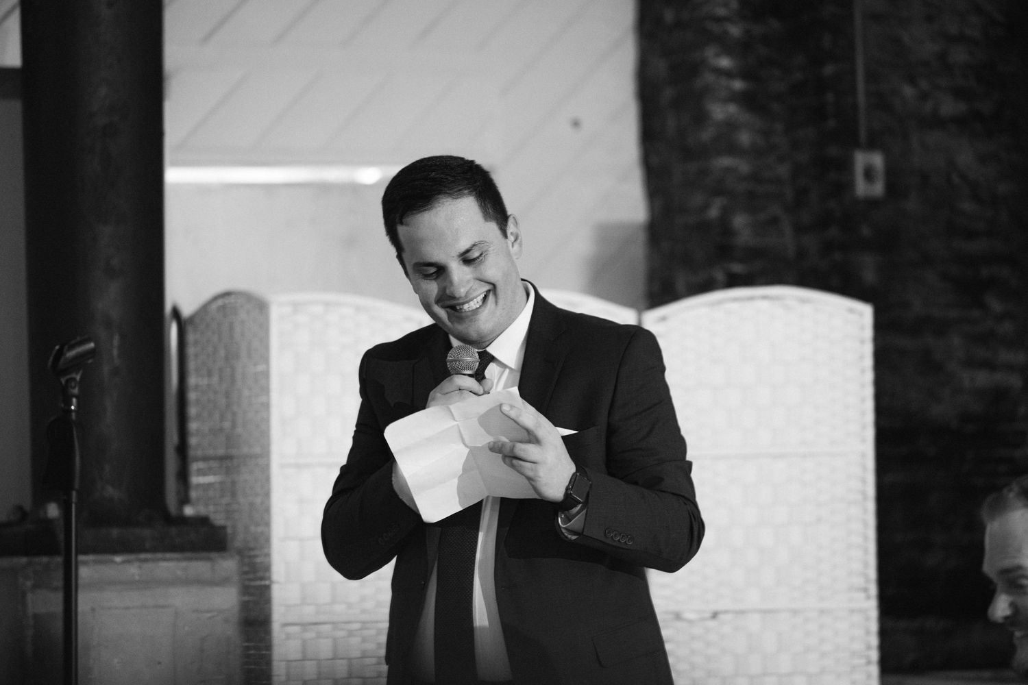 Black and white photo of a person in a suit laughing while looking at their cell phone during an event.