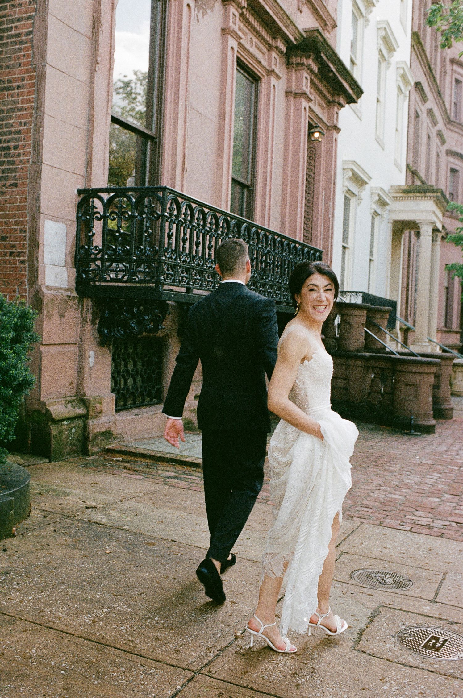 A candid wedding photo on a historic brownstone street with ornate iron railings.