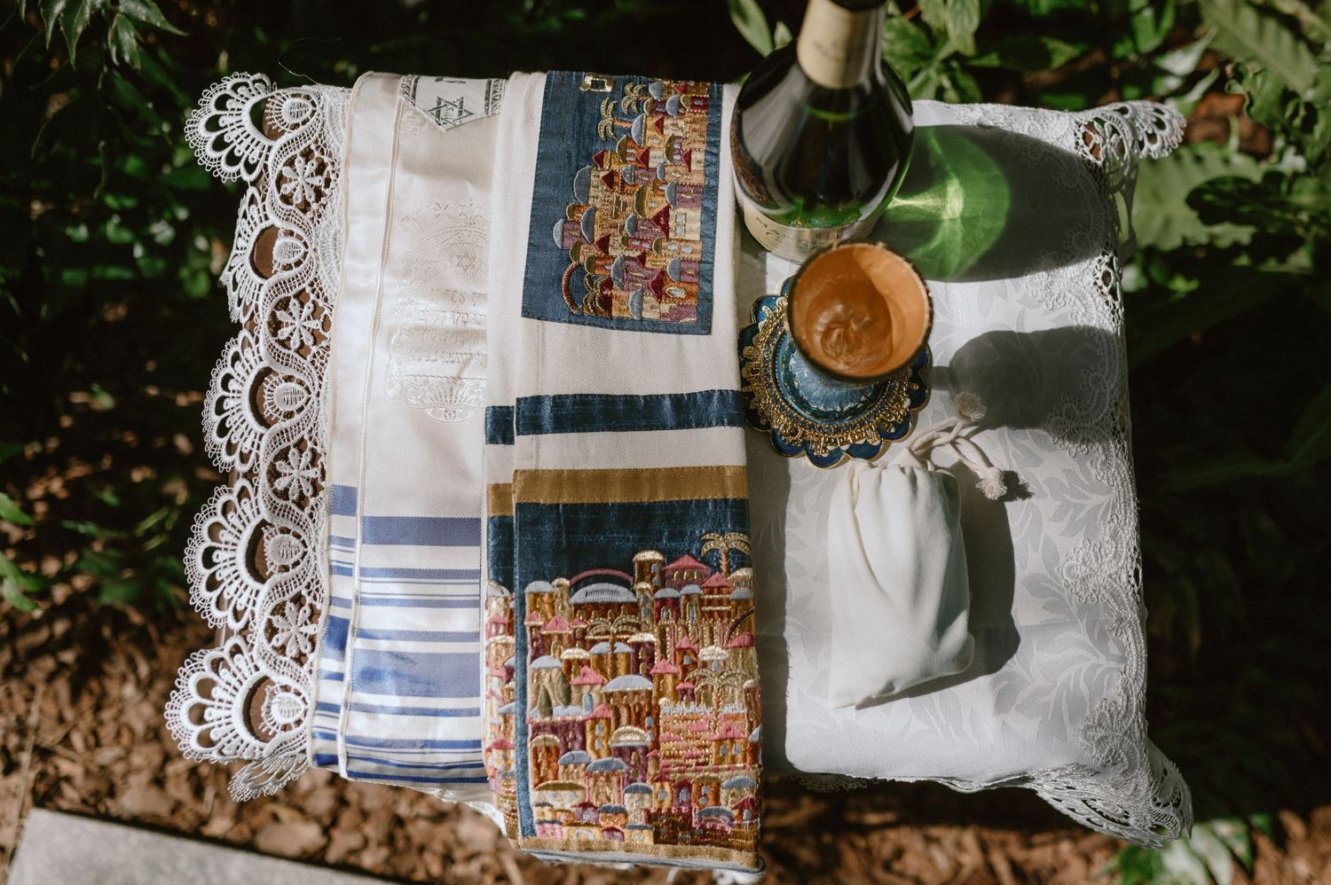 Vintage lace tablecloth and decorative textiles arranged with glass bottle in natural sunlight.
