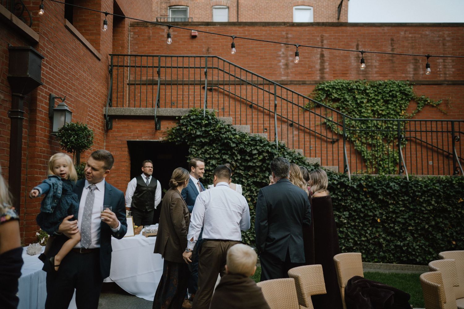 Wedding guests mingling in an ivy-covered brick courtyard during an outdoor reception.