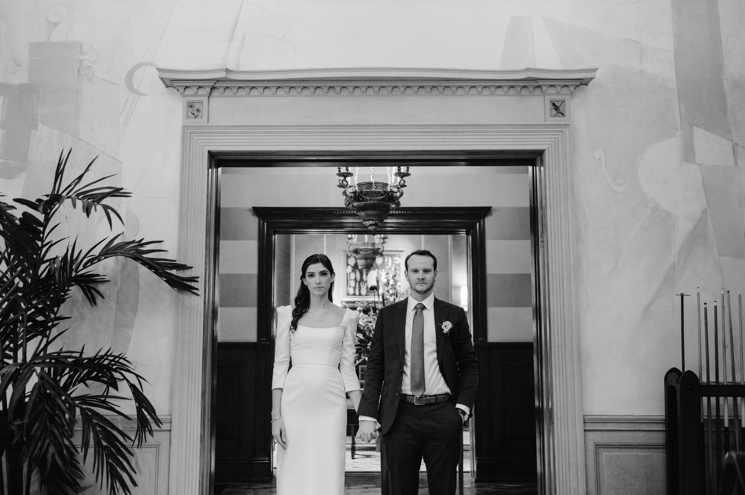 Black and white wedding photo showing a couple standing in an elegant doorway.