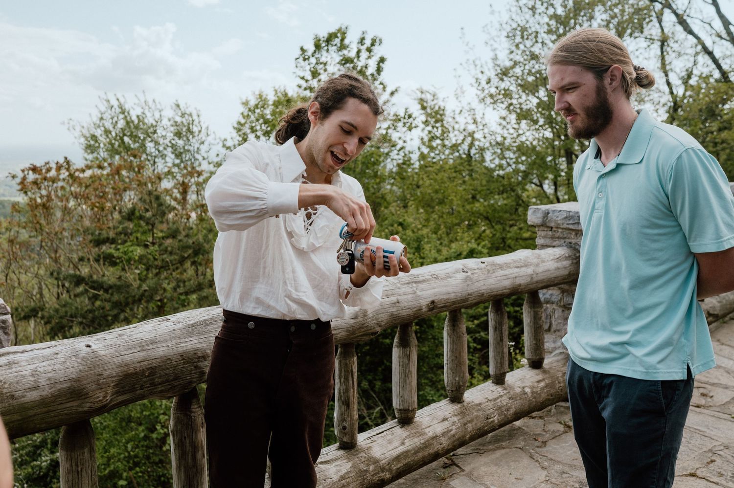 Two friends sharing laughs while having drinks on an outdoor wooden deck.