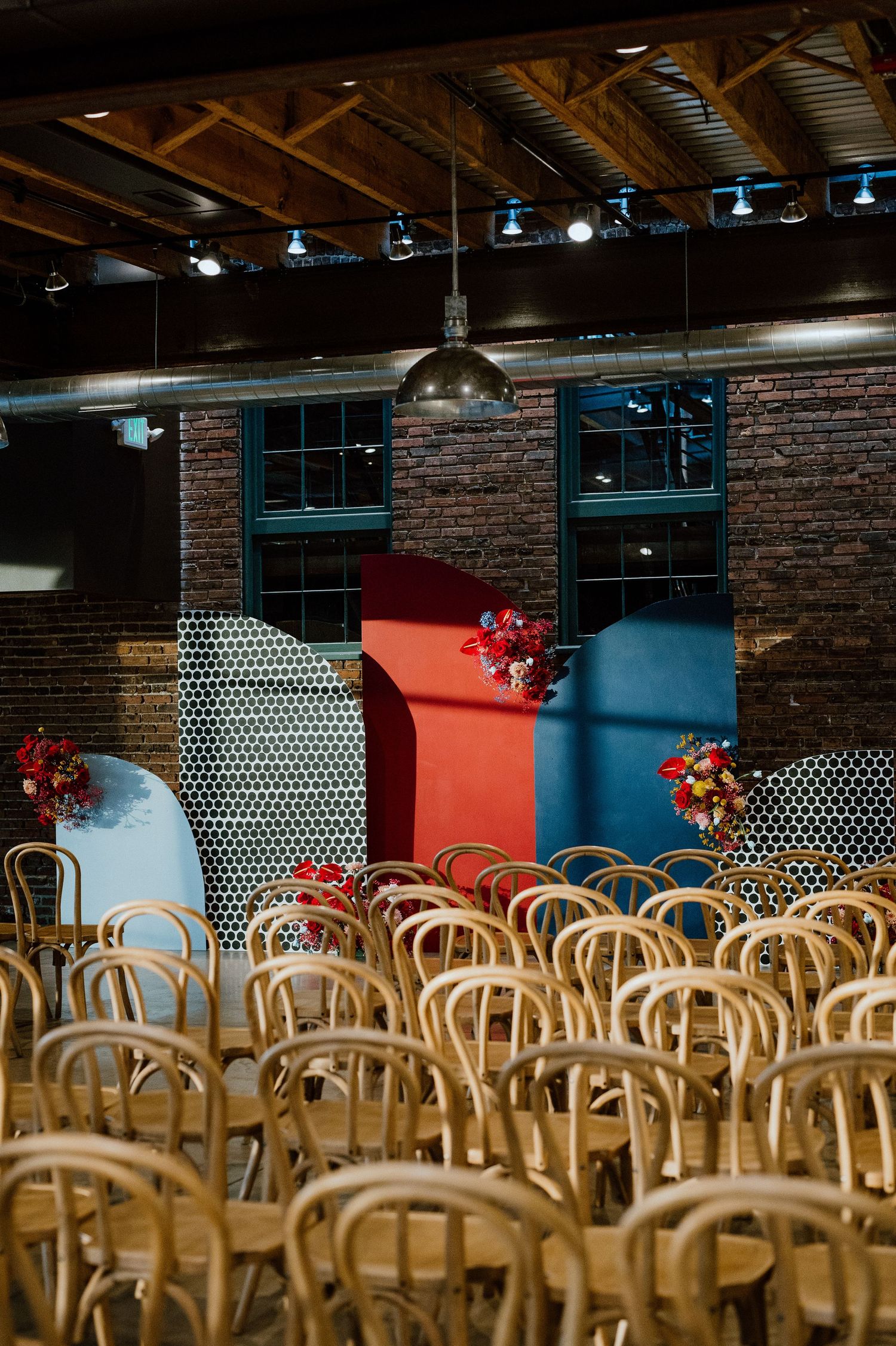 Rustic indoor venue with wooden chairs and colorful backdrop against exposed brick walls.