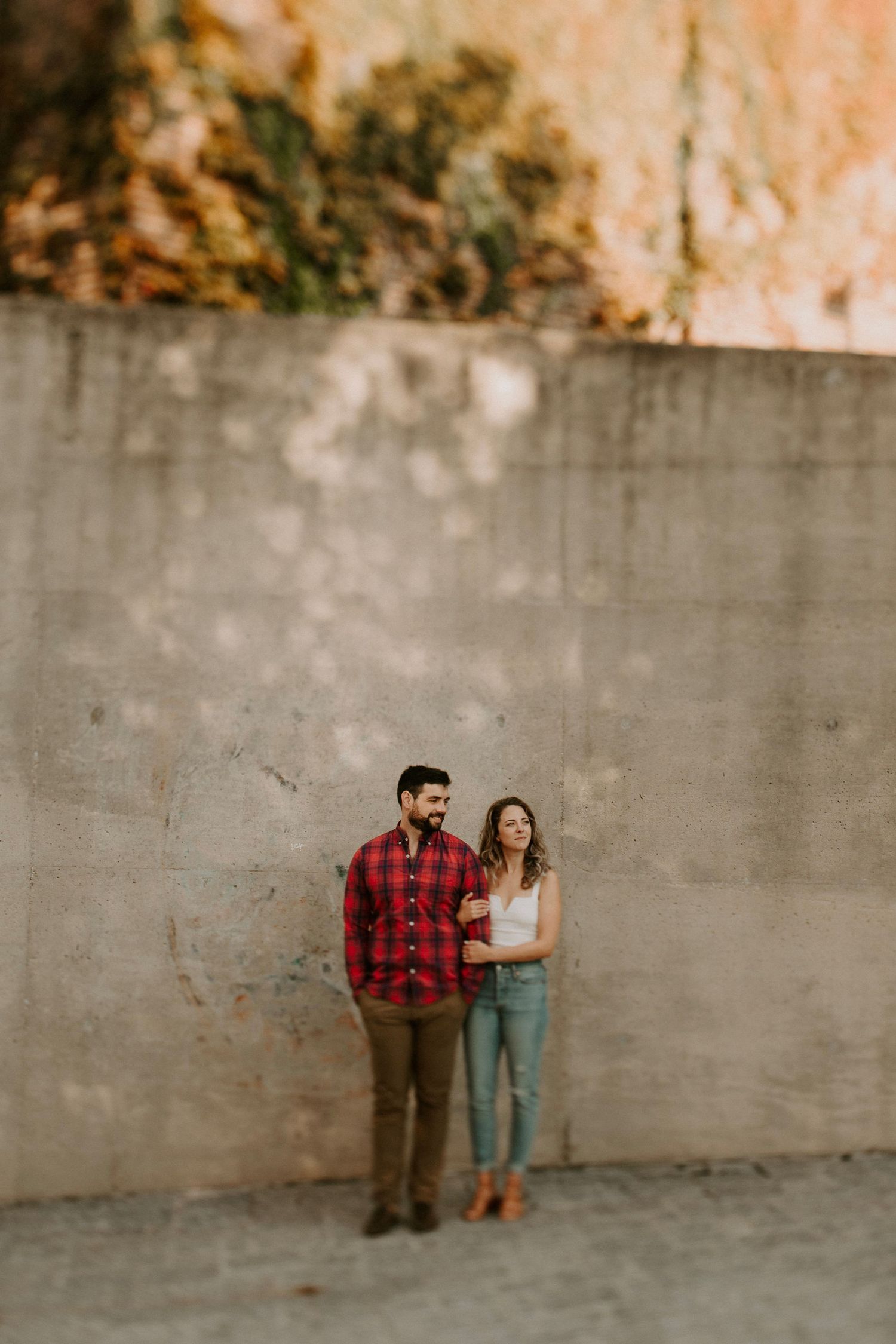 Romantic couple pose against grey wall in urban setting with plaid and denim outfits.