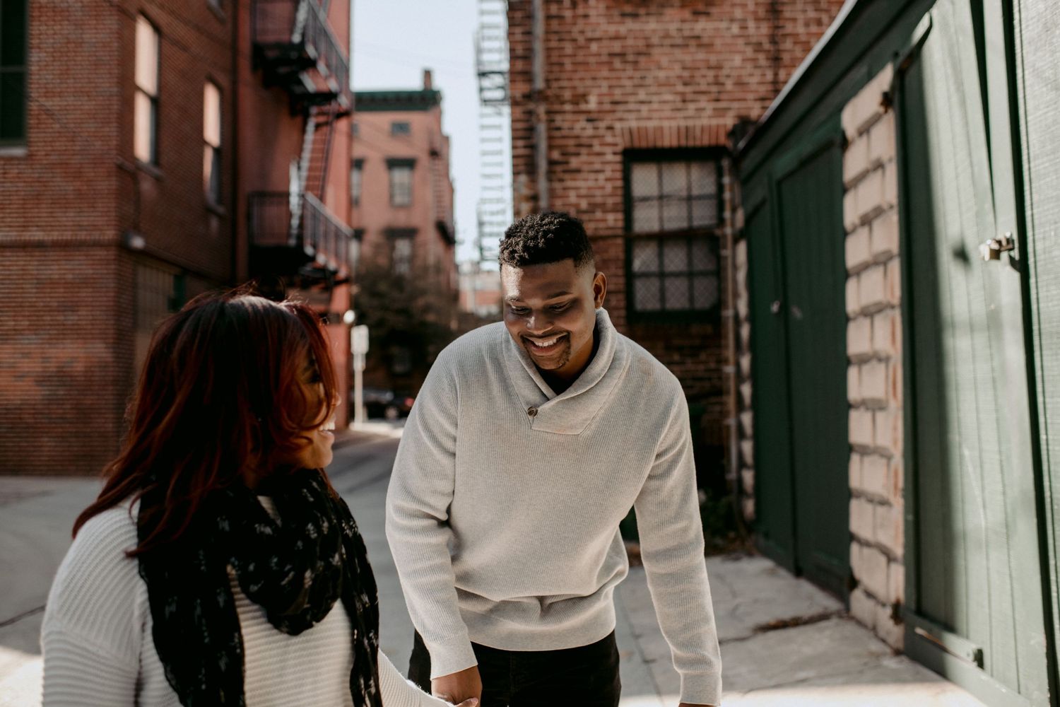 A couple in casual winter wear converses on a city street.