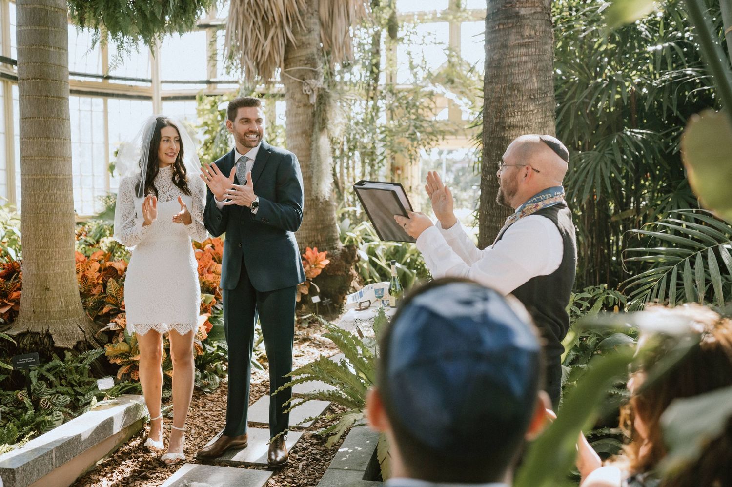 Wedding ceremony taking place in a bright greenhouse surrounded by tropical plants.
