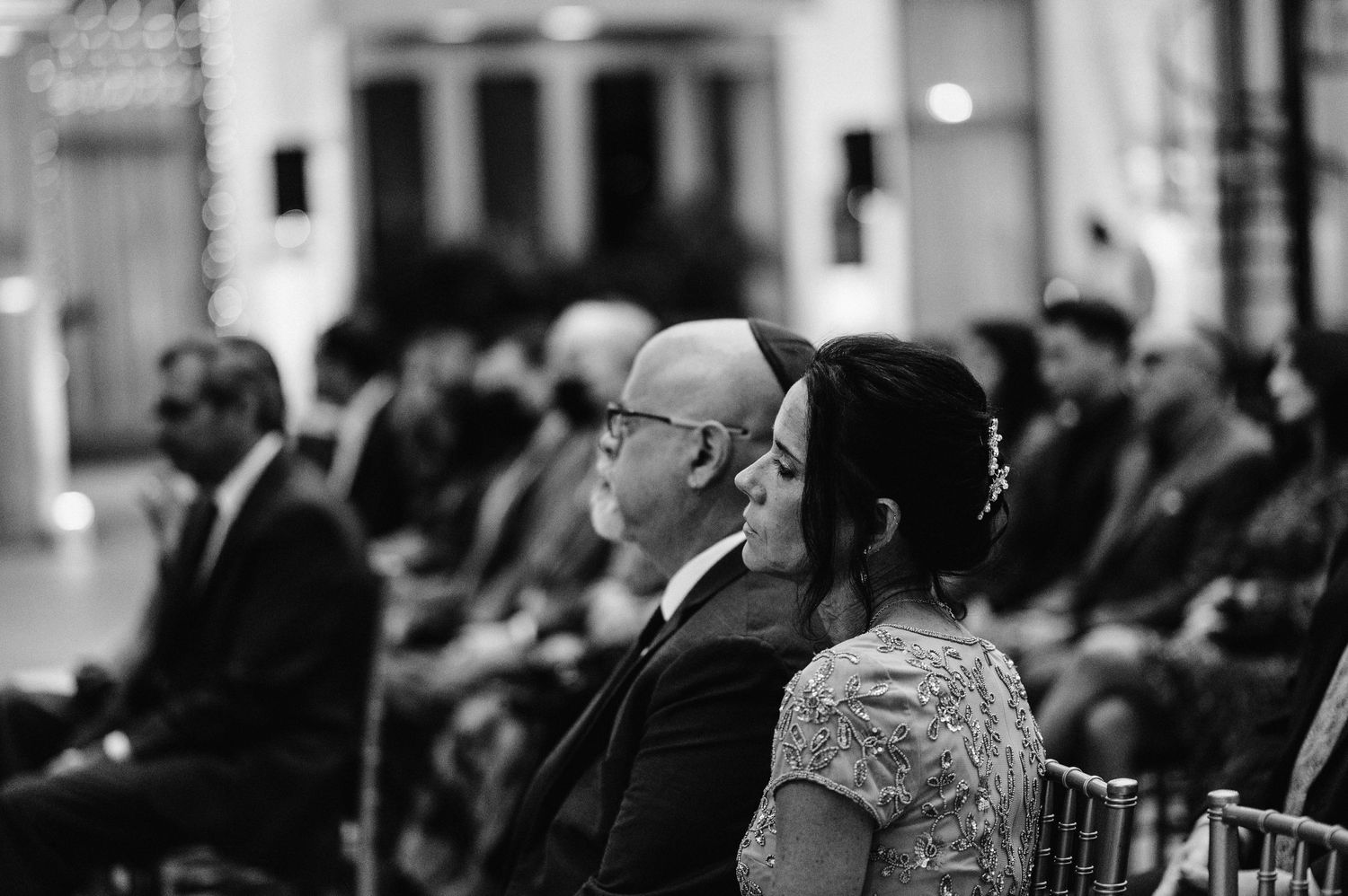 Black and white photo of wedding ceremony guests seated in formal attire.