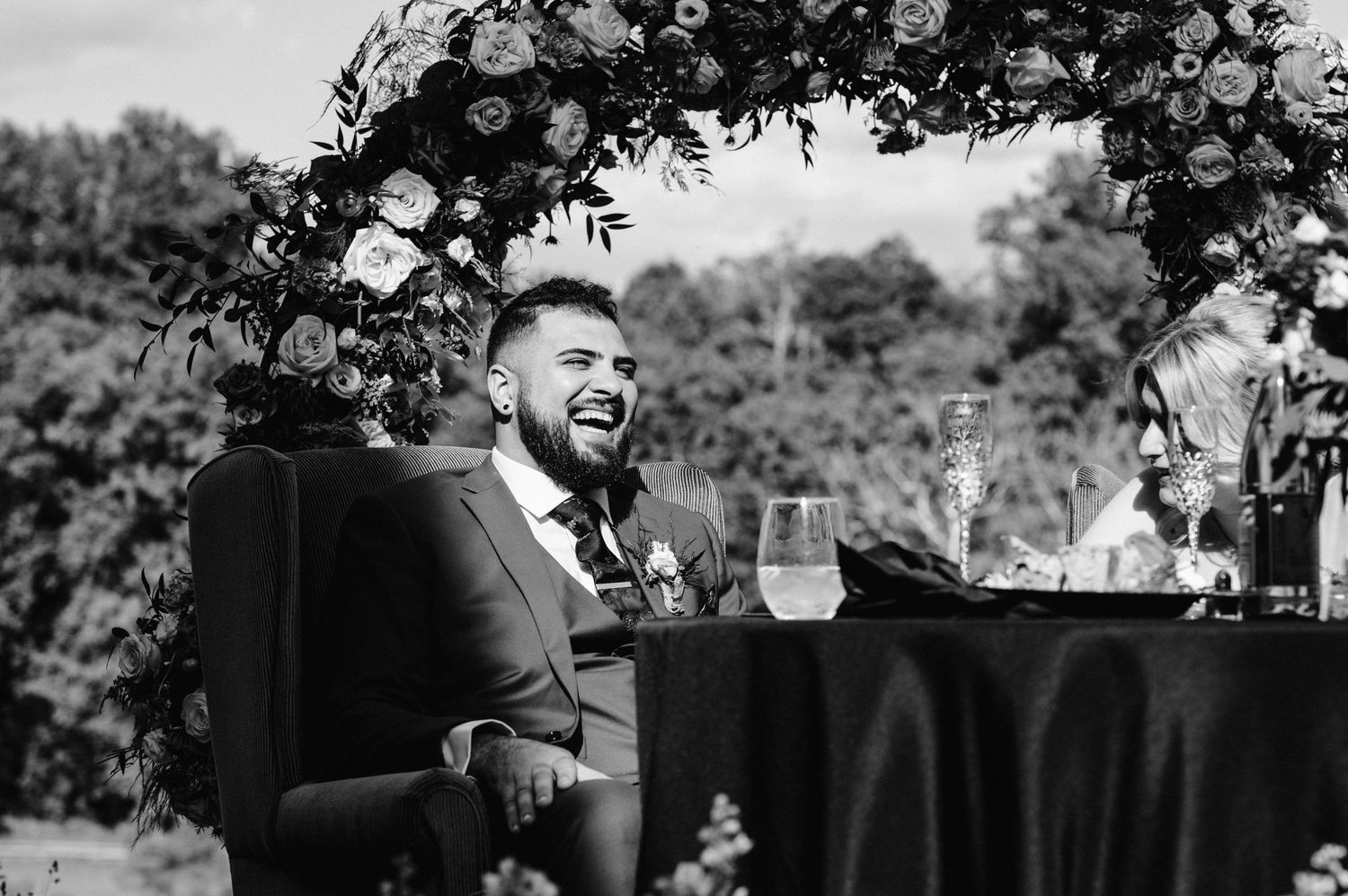 Guest laughs joyfully during wedding reception under floral arch and string lights.