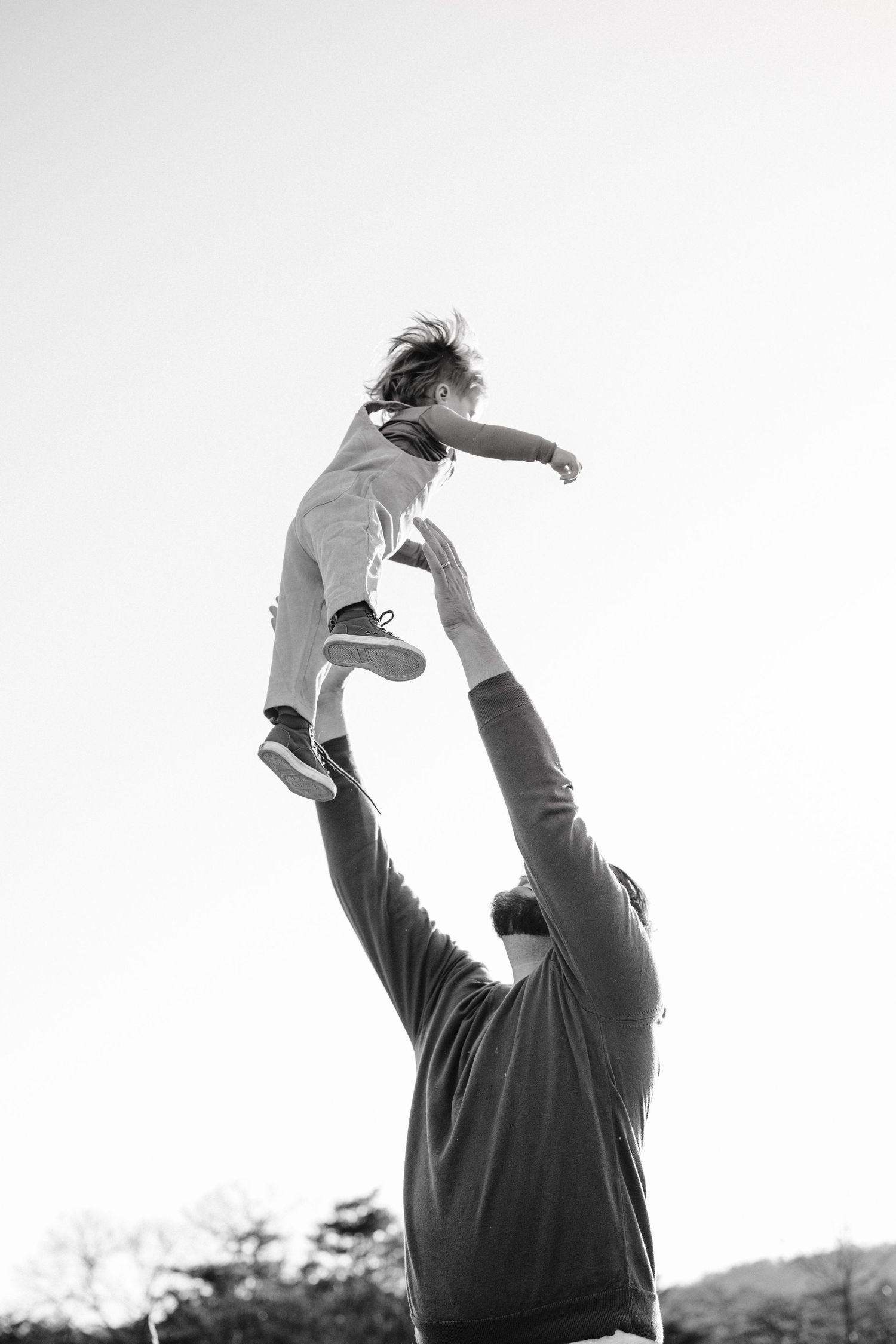 A dramatic black and white shot of a child being playfully lifted high into the air.