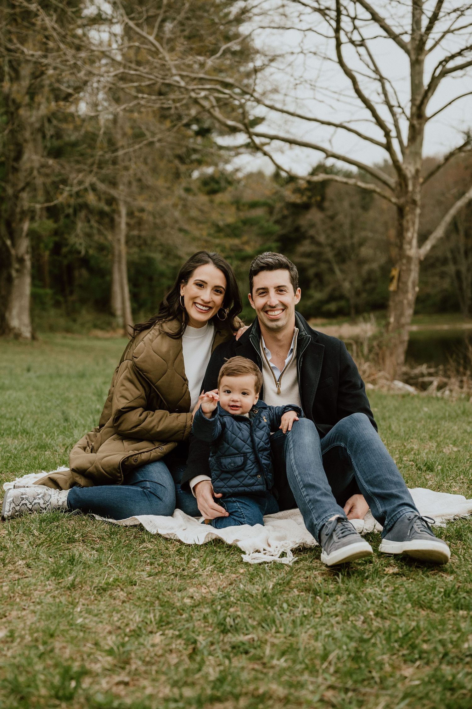 Family sitting together on blanket in park during autumn photoshoot.