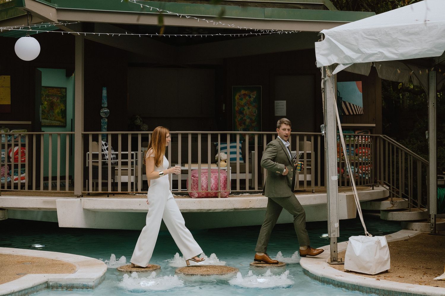 People walking along a wooden deck by a pool during an outdoor event.