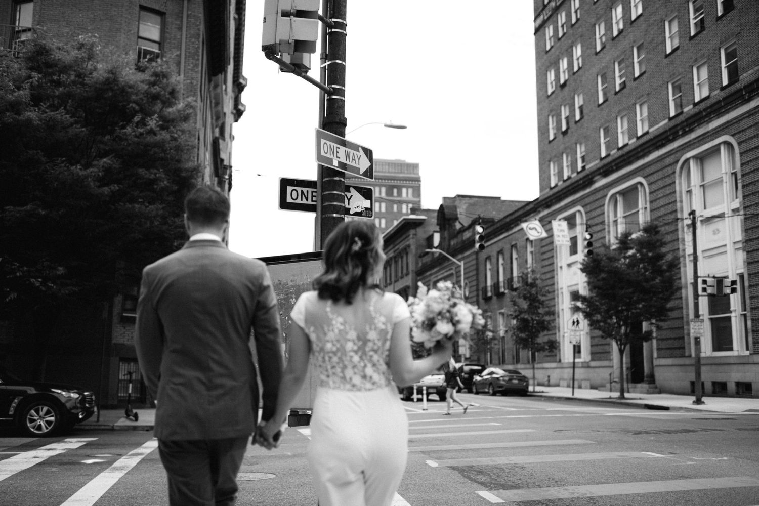 Black and white photo of newlyweds walking down city street corner.