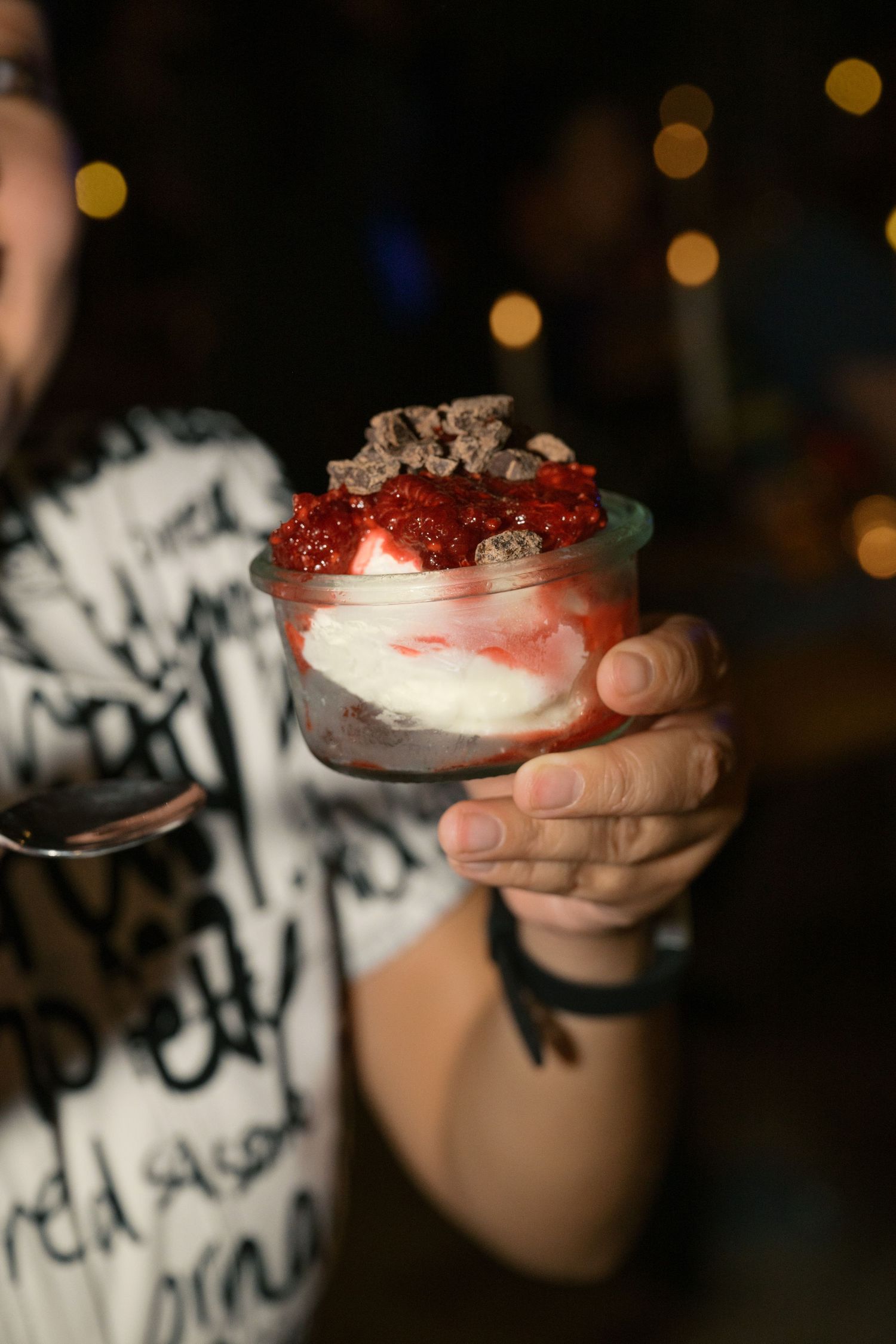 Close-up of hands holding a layered dessert with strawberries and cream in a glass.