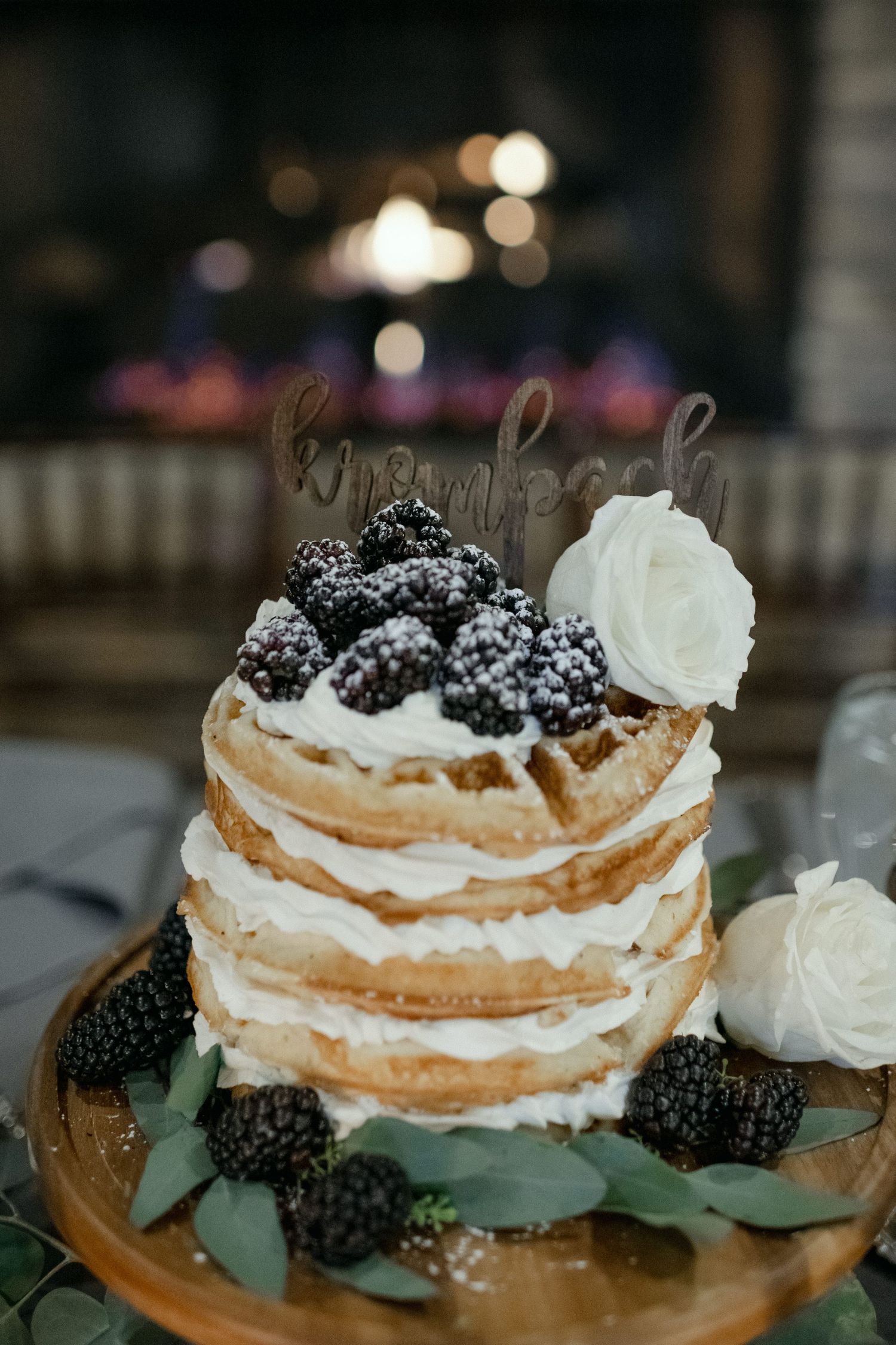 Close-up of a naked wedding cake topped with fresh blackberries and white flowers.
