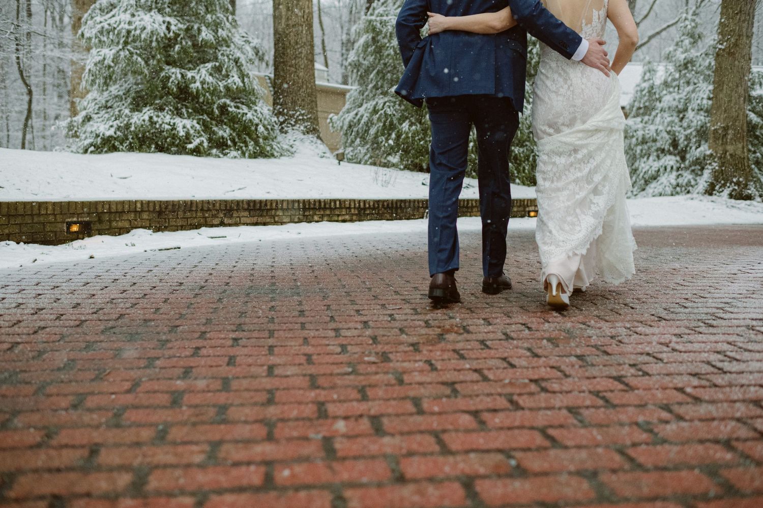 A cropped view shows a couple's legs and formal attire on a snow-dusted brick pathway.