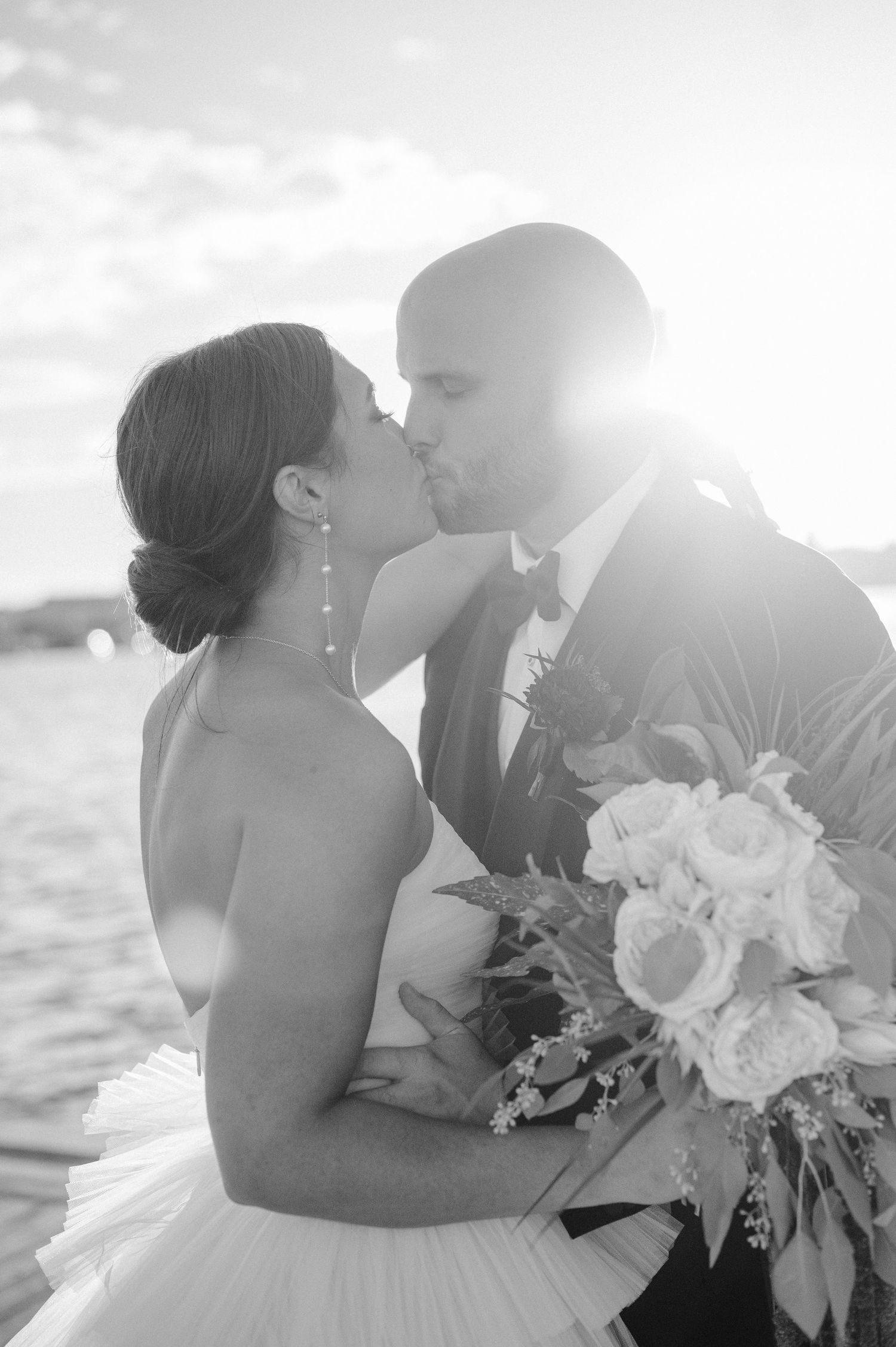 Intimate black and white wedding portrait with couple sharing a kiss while holding floral bouquet.