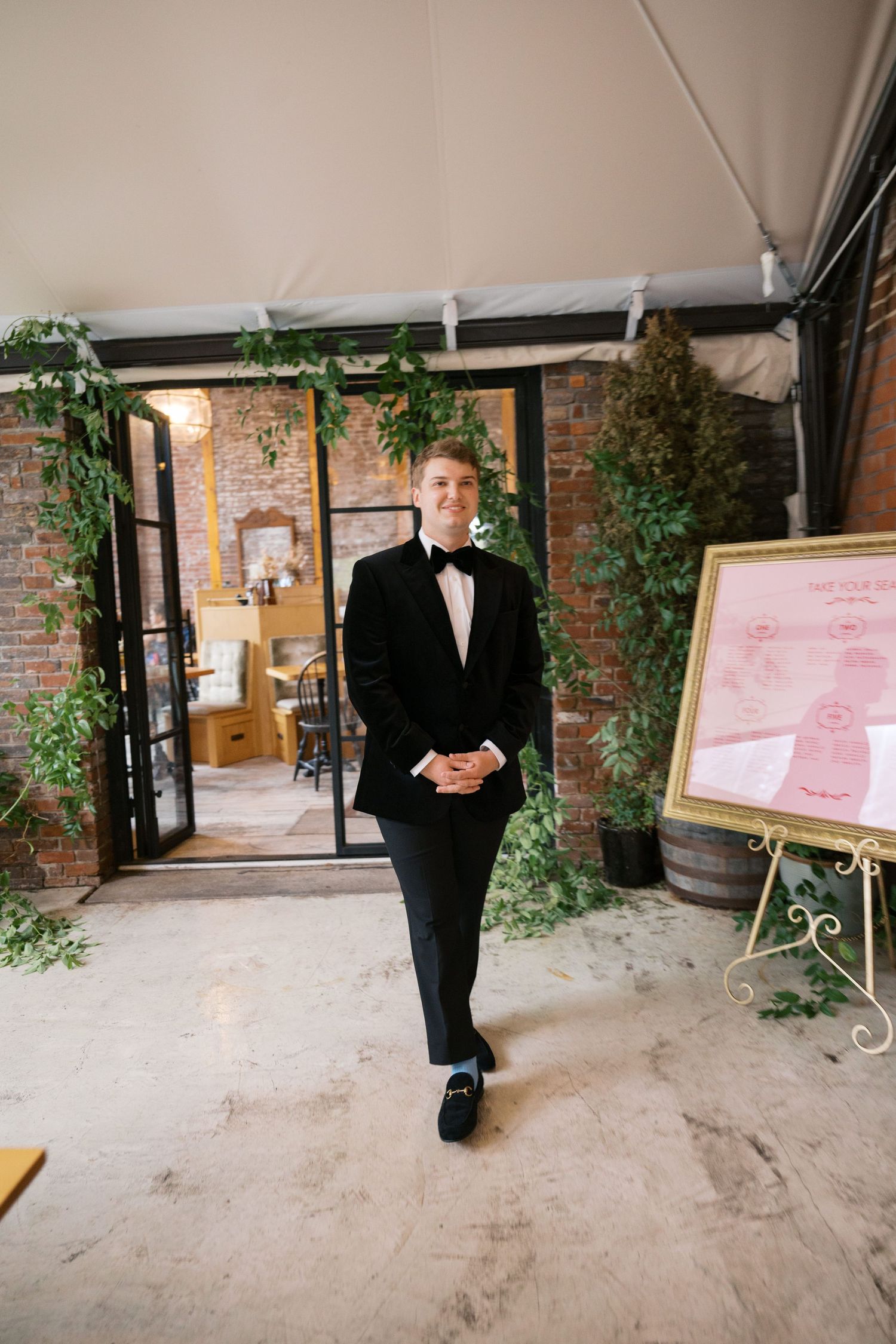Formal wedding attire on display in an industrial-style venue with exposed brick and greenery.