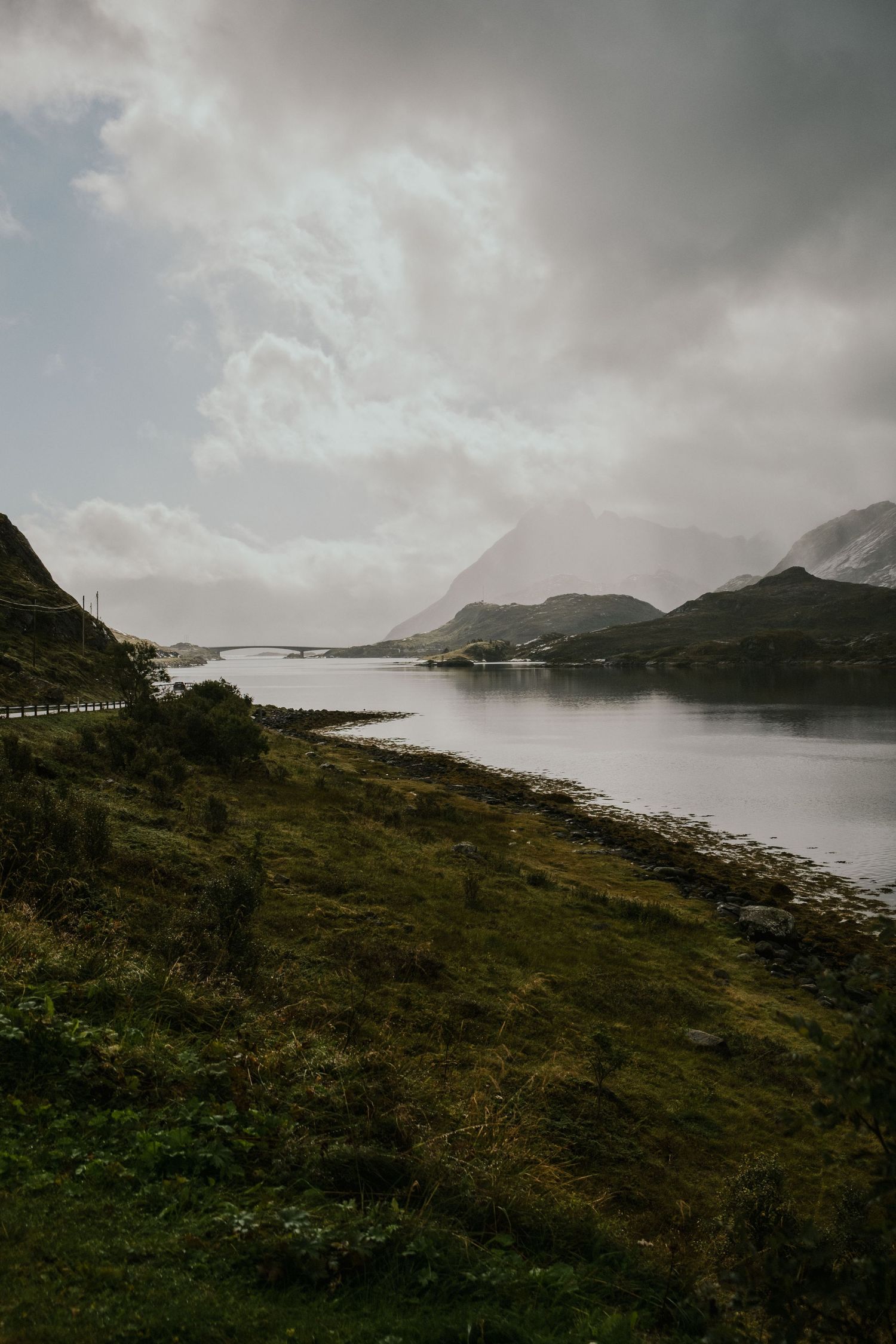 Moody landscape of a serene lake surrounded by mountains under cloudy skies in a remote wilderness setting.