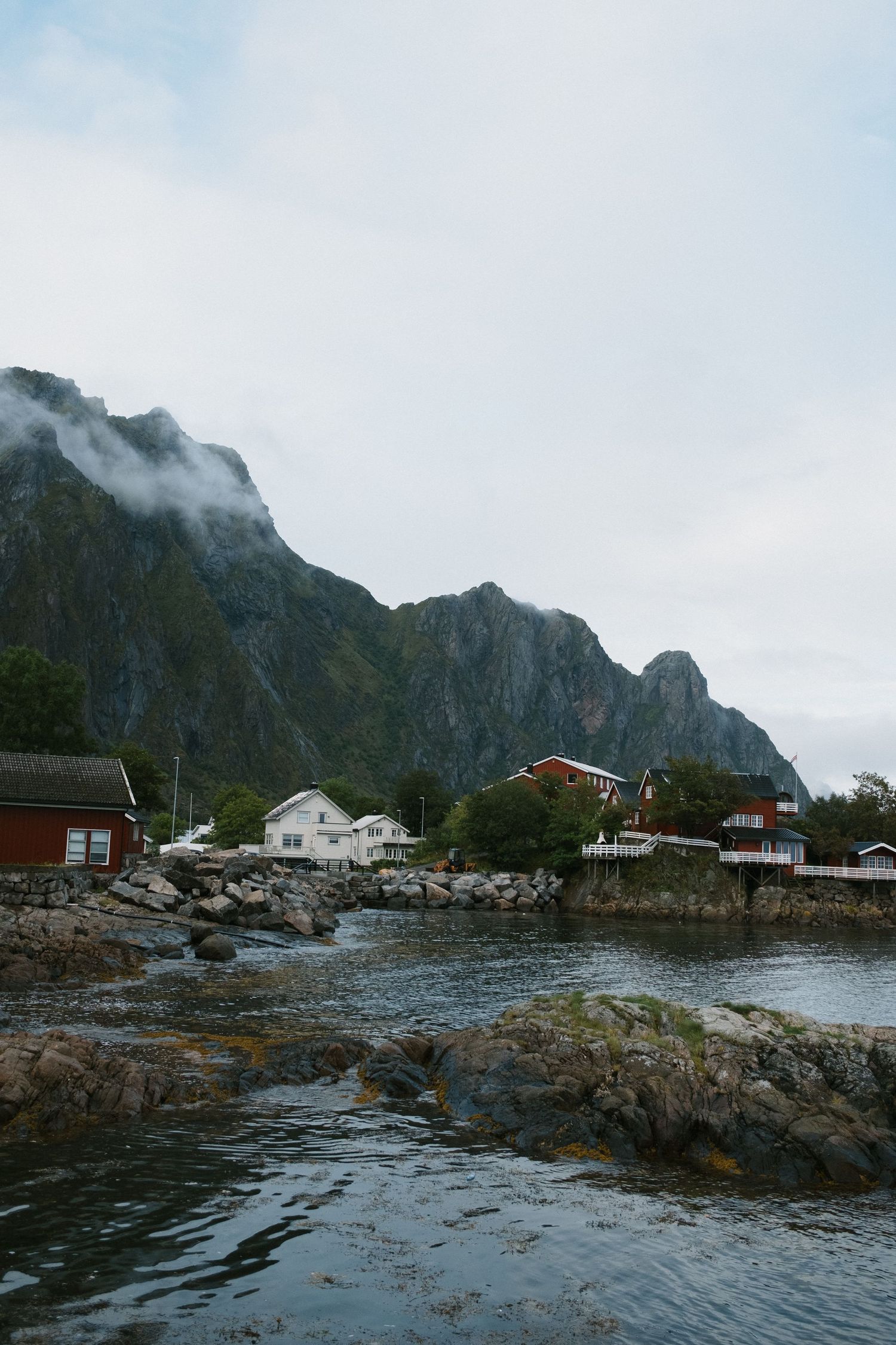 Coastal houses nestled among rocks with towering mountains rising behind them.