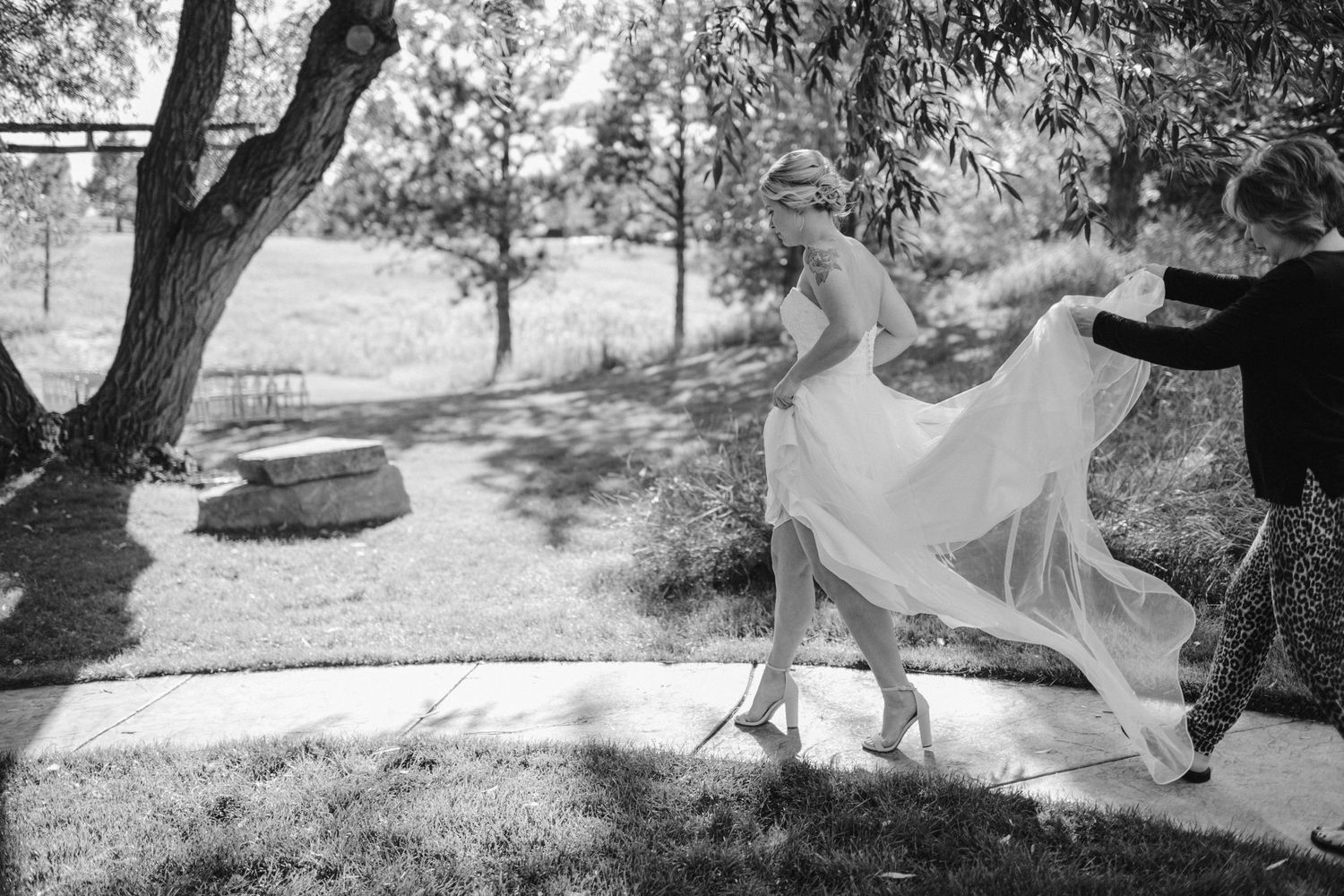 A flowing wedding dress moves gracefully in a sunlit outdoor garden setting.