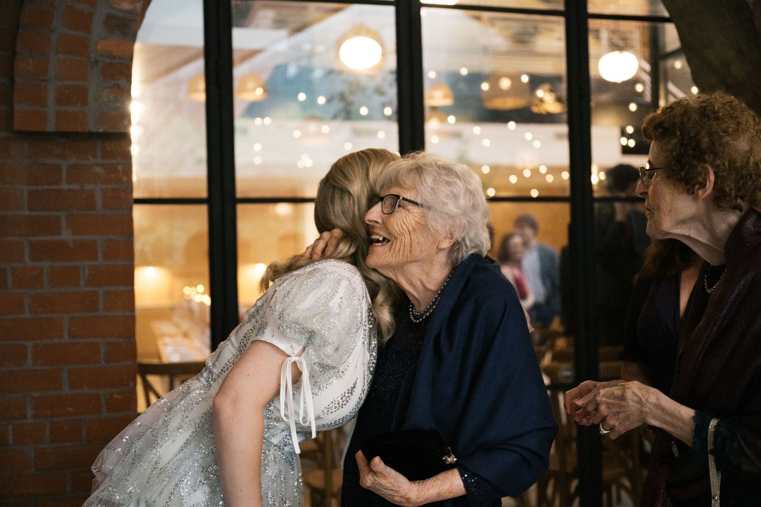 Emotional wedding moment captured through window panes with twinkling lights in background.
