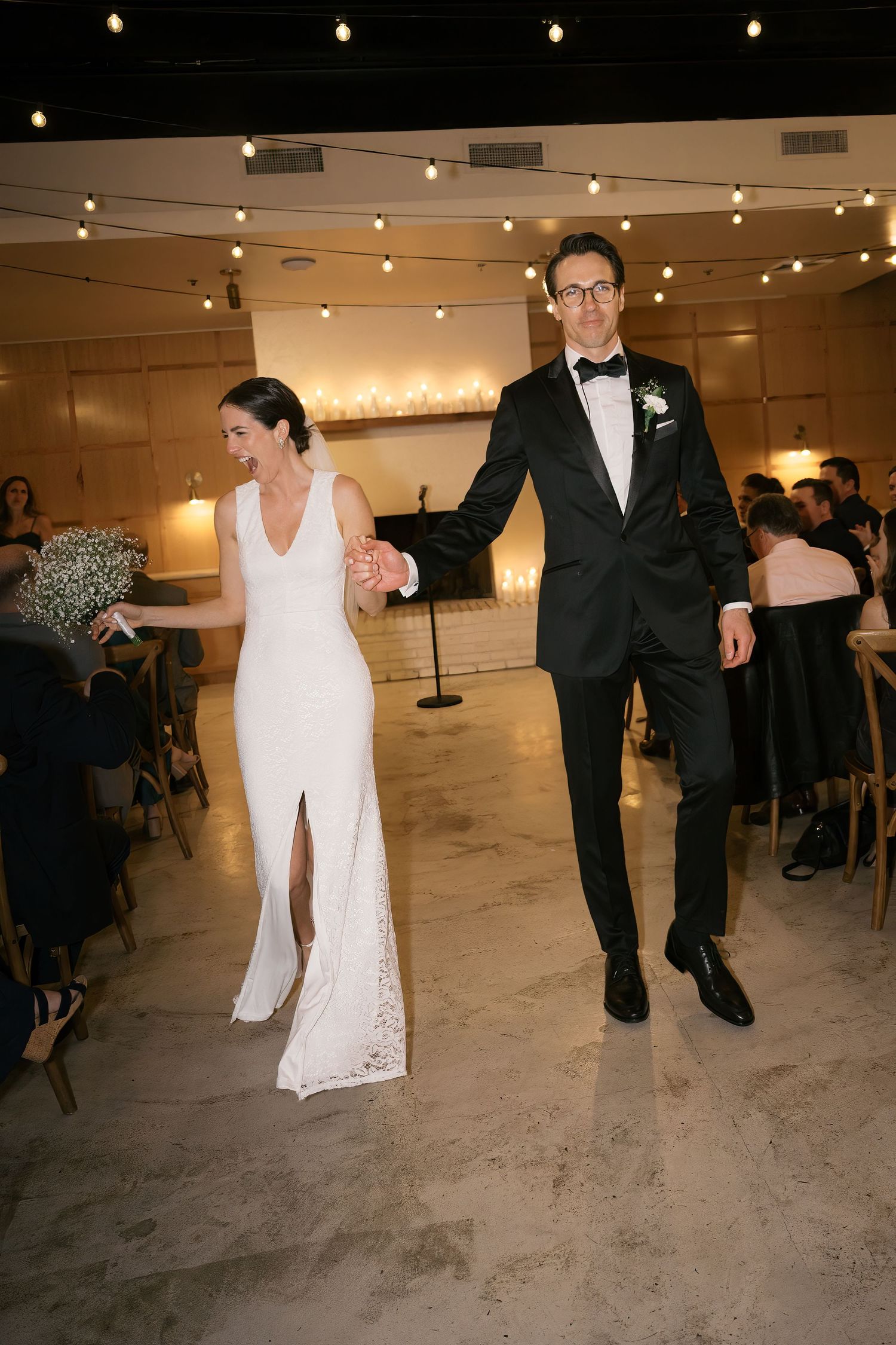Newlywed couple makes their grand entrance at reception venue with twinkling string lights overhead.