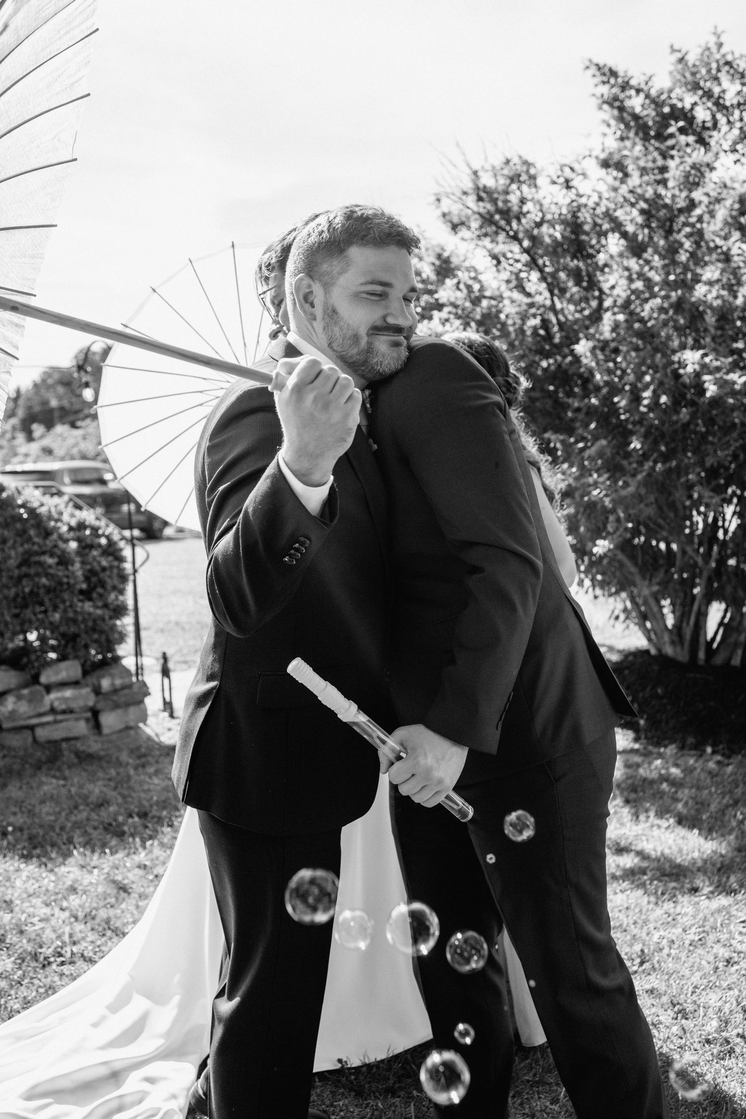 Two people share an emotional moment with parasols at an outdoor wedding.