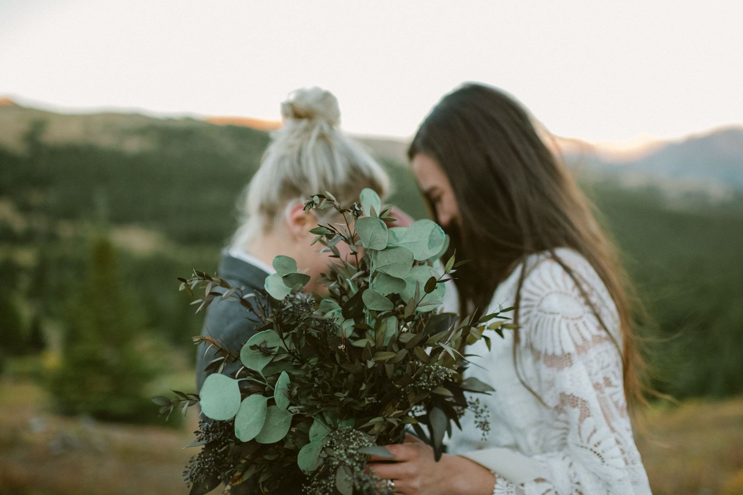Two people examine a fresh bouquet of eucalyptus branches against mountain backdrop at dusk.