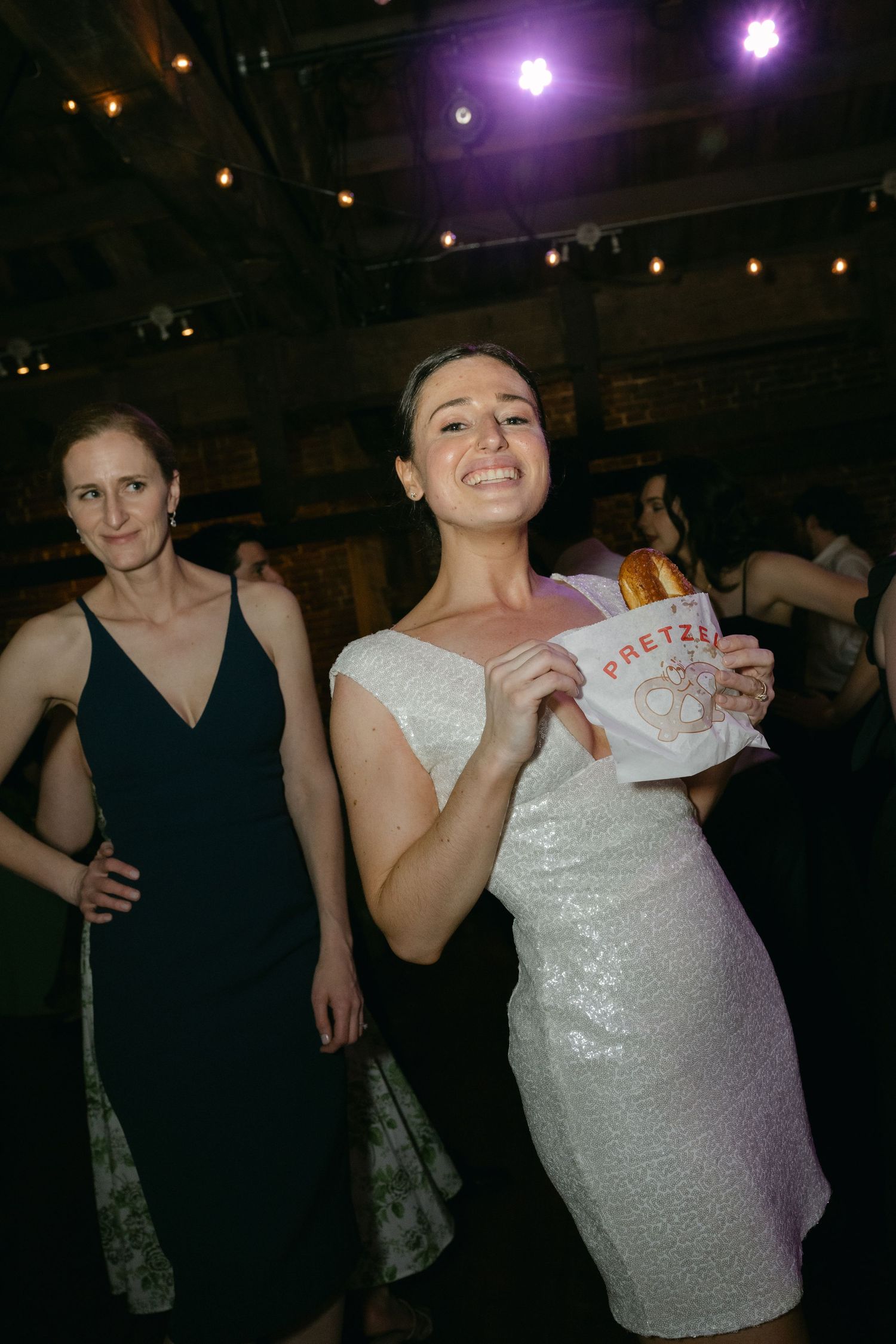 Party guests in formal attire dance and celebrate at an indoor reception venue with purple mood lighting.