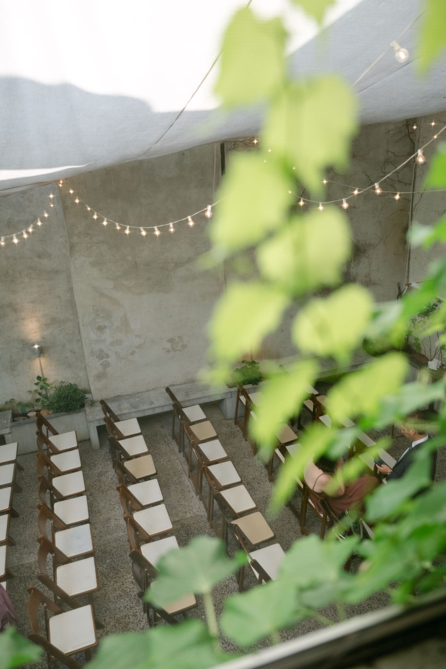 String lights hang over rows of white chairs in an outdoor wedding ceremony space.
