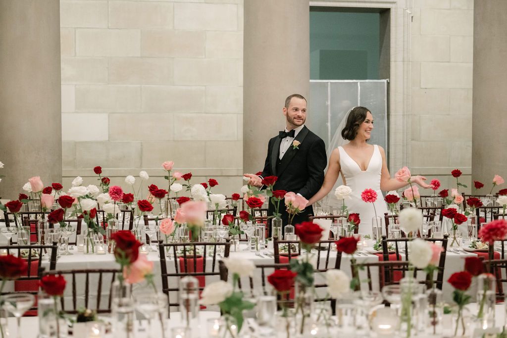 A wedding reception hall decorated with white linens and red floral centerpieces on long banquet tables.
