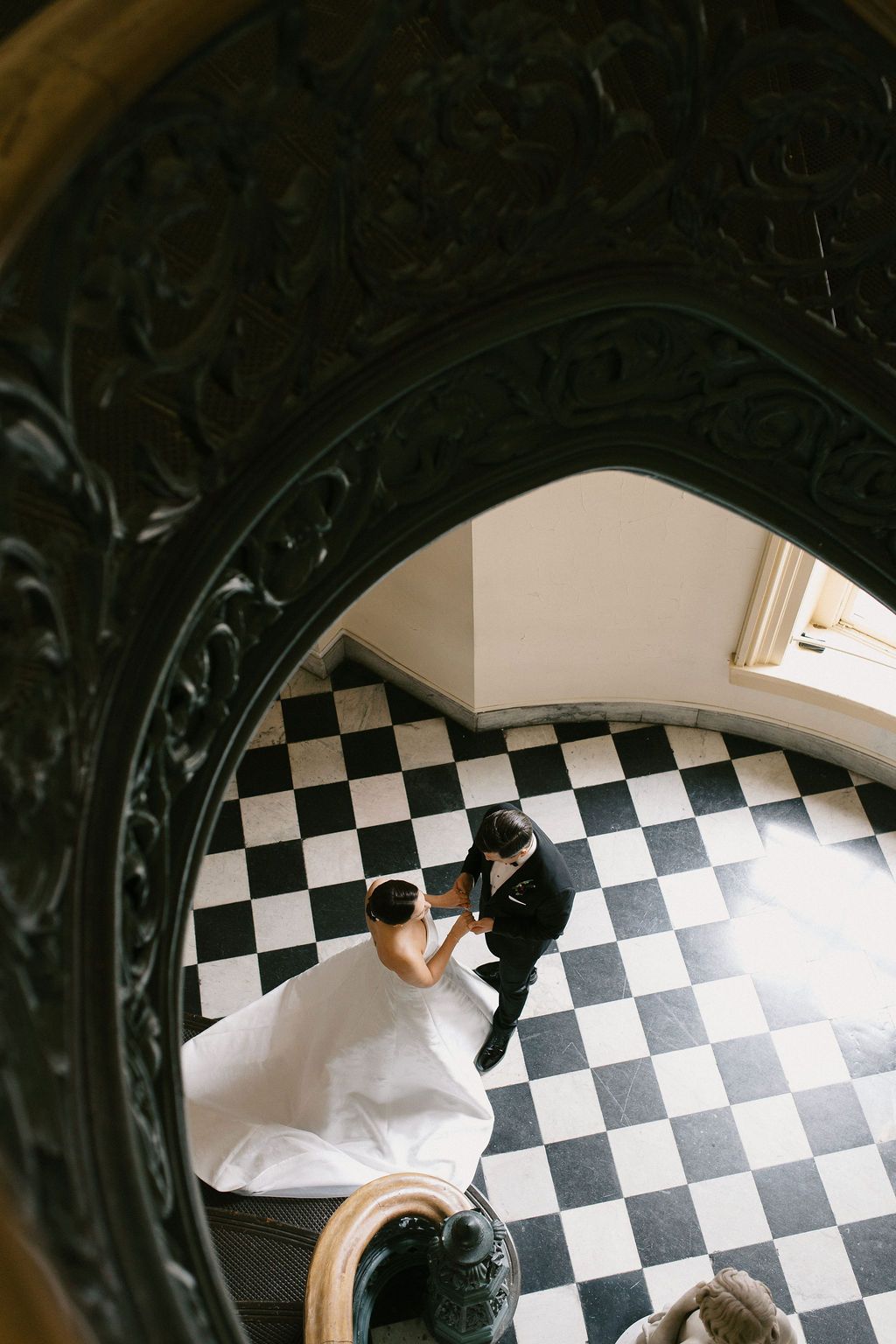 Overhead view of bride and groom on dramatic black and white checkered floor.