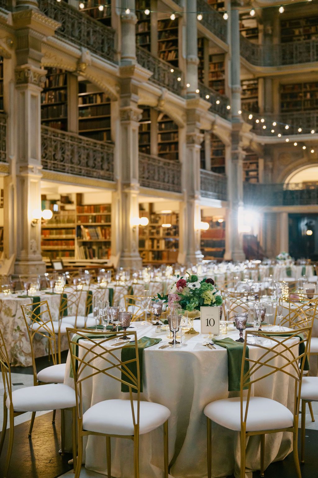 Elegant wedding reception setup in a grand historic library with string lights and gold chairs at George Peabody Library Wedding in Baltimor